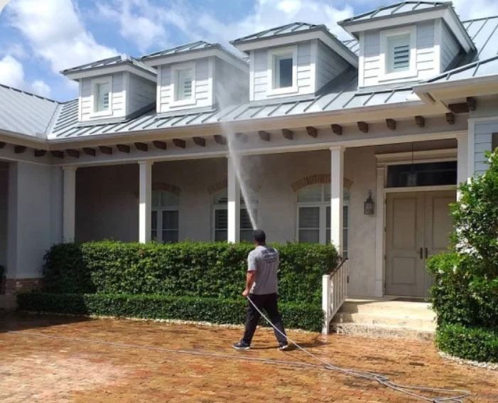 A man is cleaning the driveway of a house with a hose.