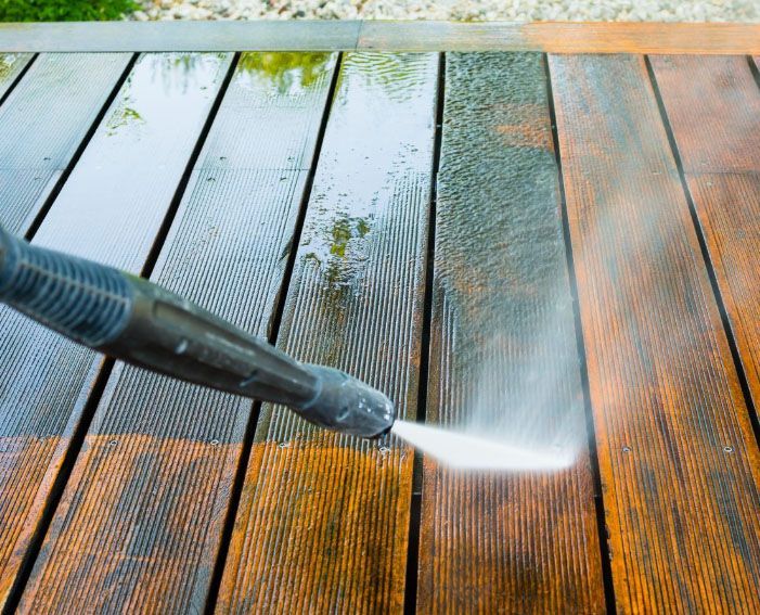 A person is using a high pressure washer to clean a wooden deck.