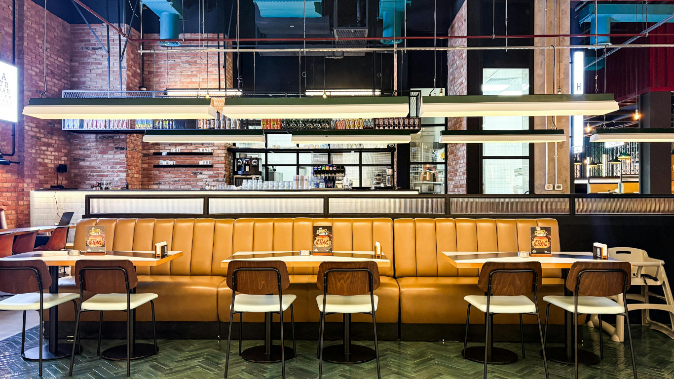 A restaurant interior featuring a long, mustard-yellow booth with matching chairs, brick walls, and modern lighting.