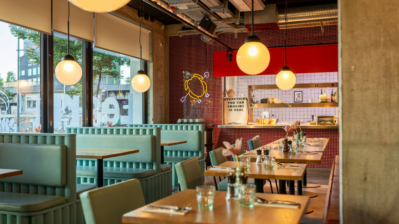 A modern restaurant interior featuring green booths, wooden tables, and glowing globe pendant lights.
