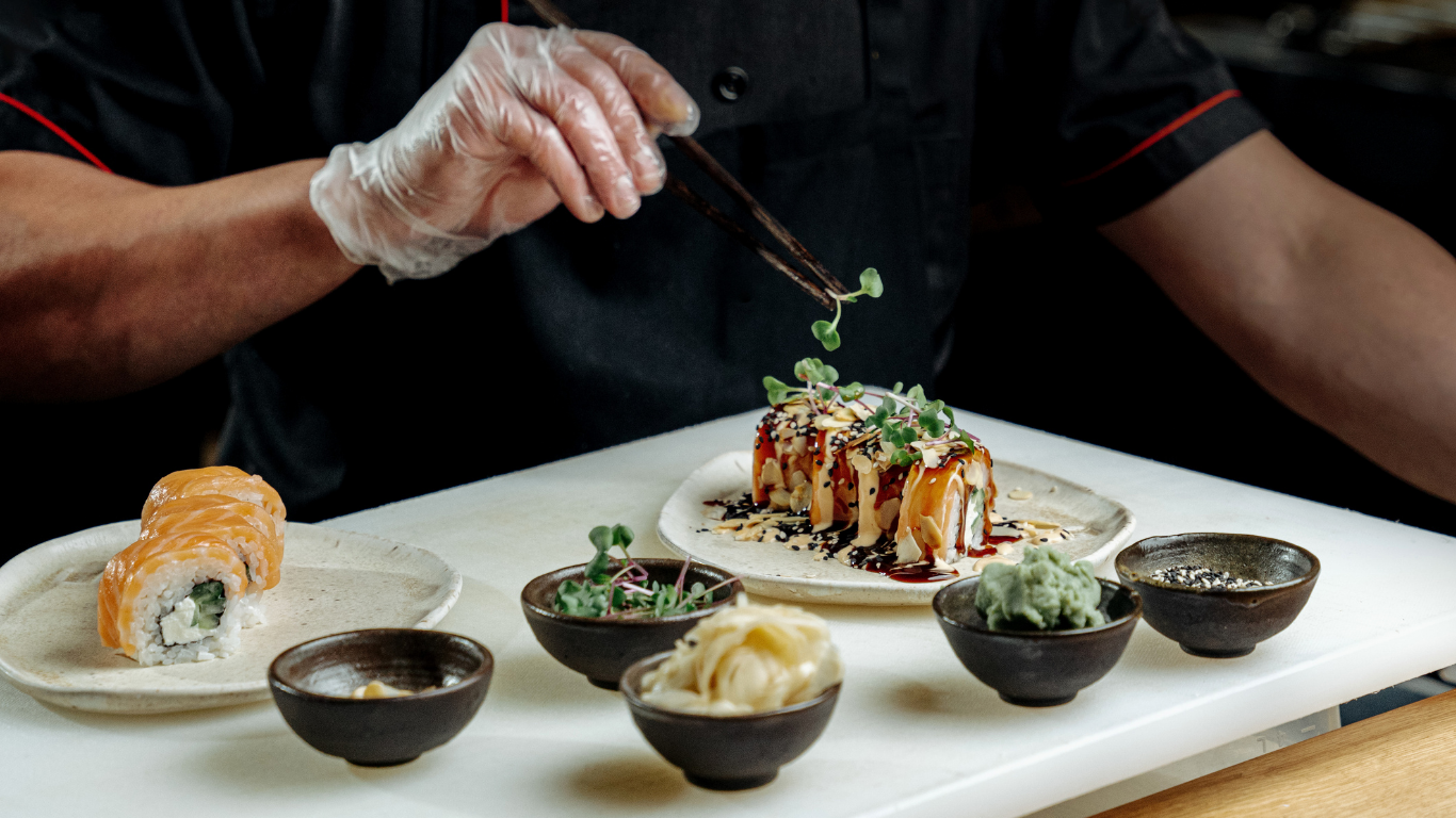 Chef plating sushi with sauces and garnishes on a white tray