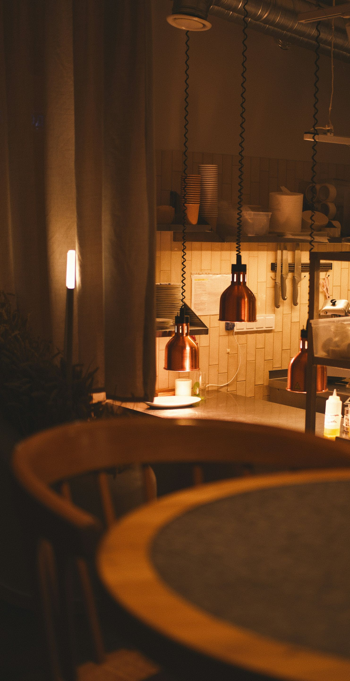 Warm-lit restaurant interior with copper pendant lights hanging over a round table.
