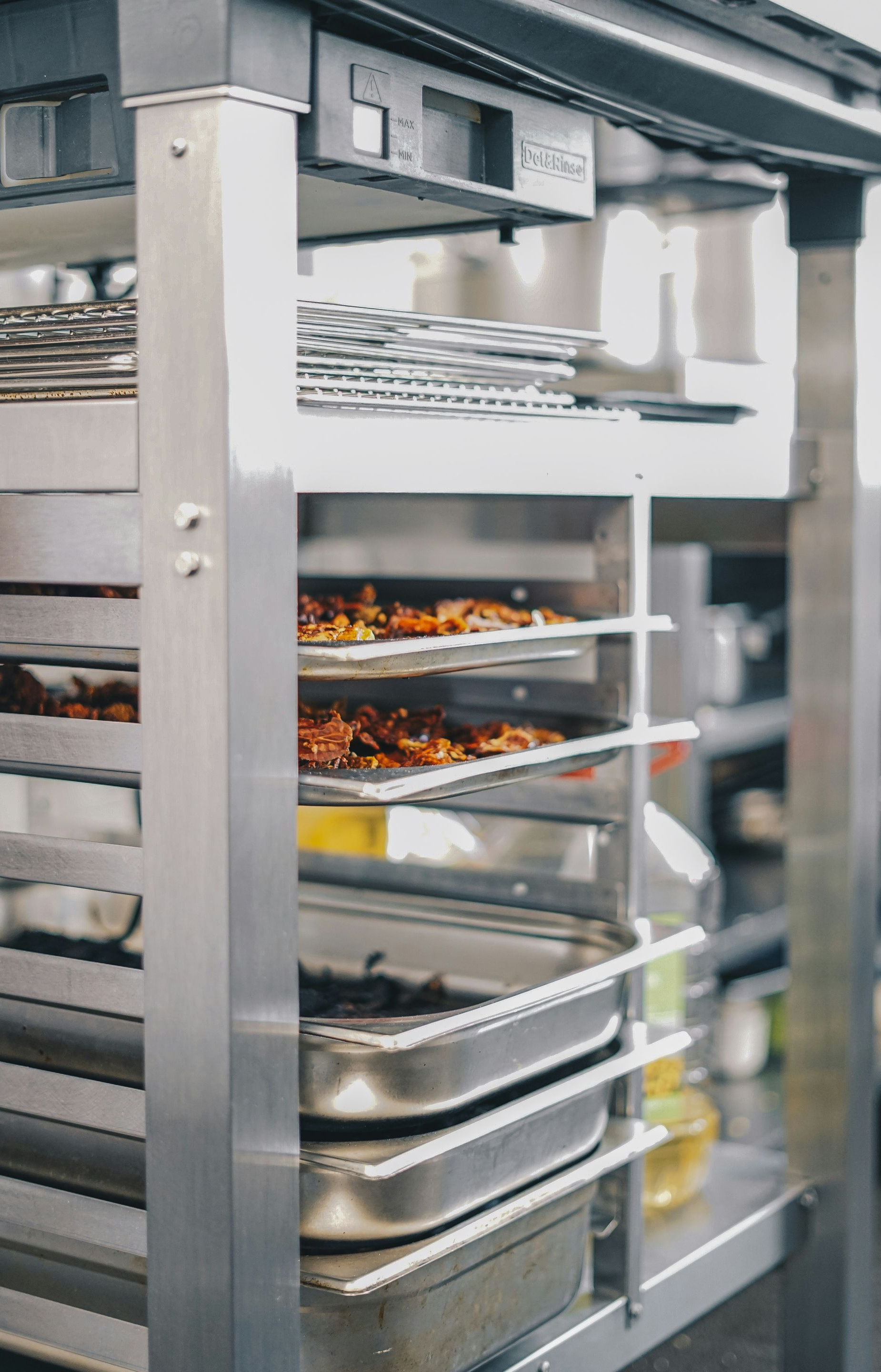 Stainless steel rack holding trays of food in a commercial kitchen.
