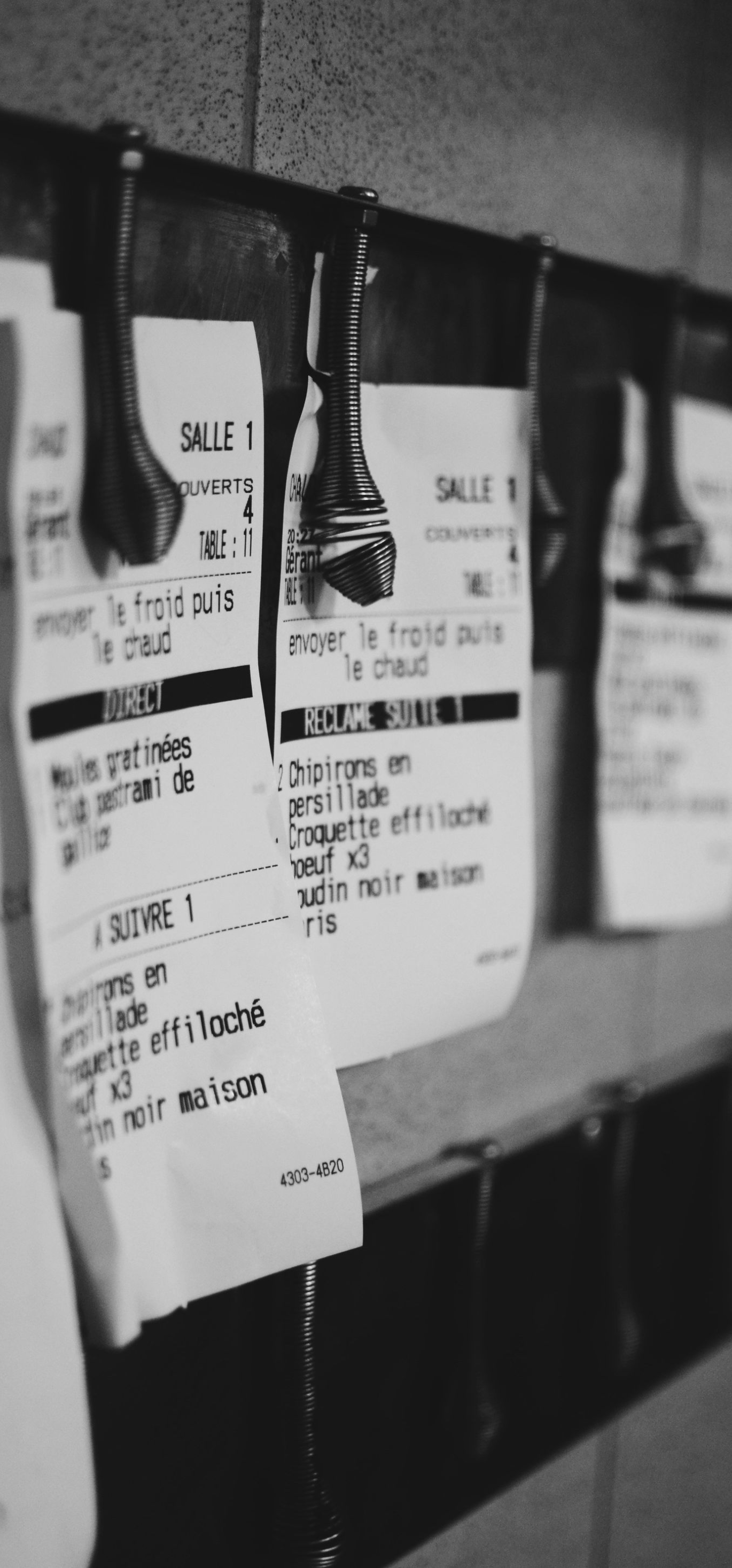 Black-and-white view of hanging luggage tags clipped to a rack in a dim indoor setting