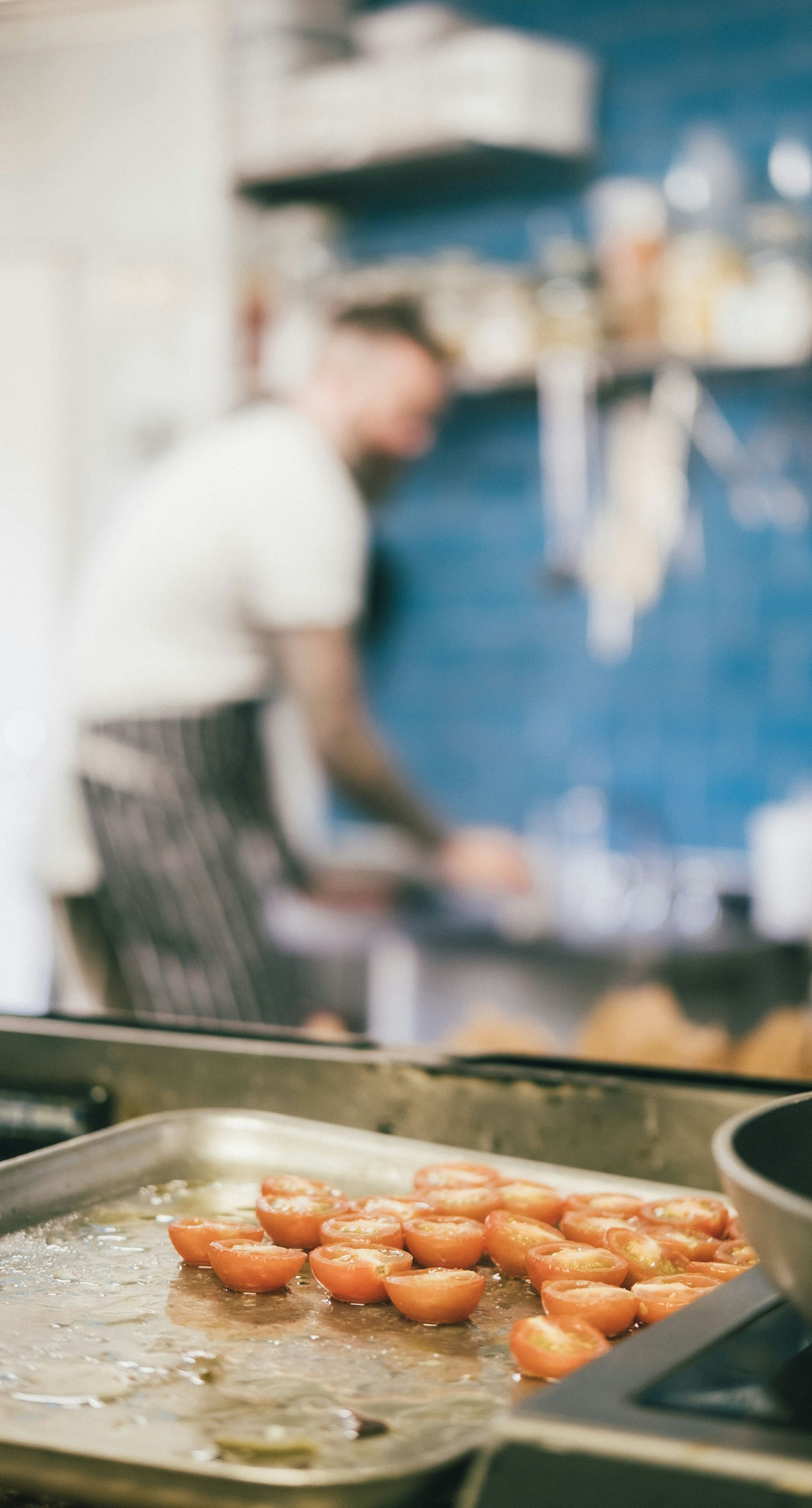 Roasted cherry tomatoes on a tray in a kitchen. Blurry chef in the background.