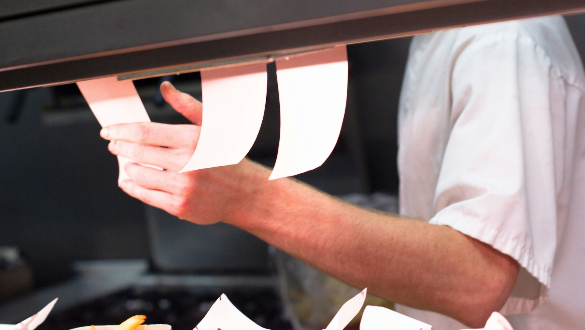 Chef's hands placing food orders on a ticket rail in a restaurant kitchen.
