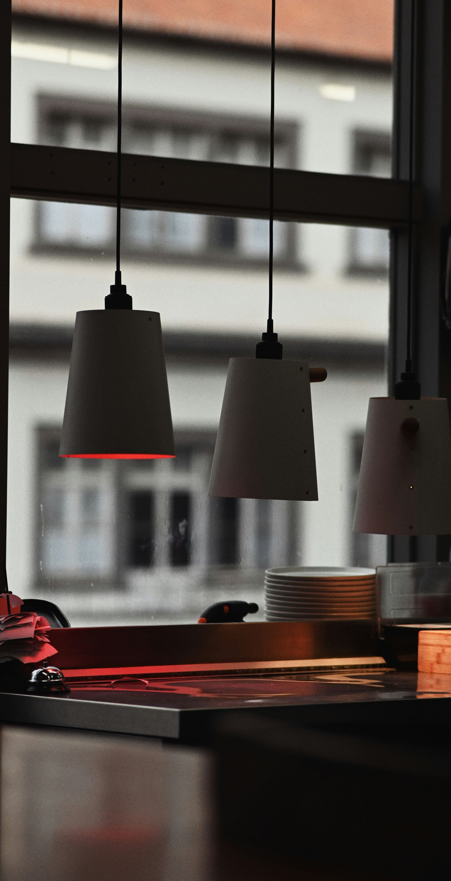 Two pendant lights illuminate a windowsill, with a blurred building visible through a window in the background.