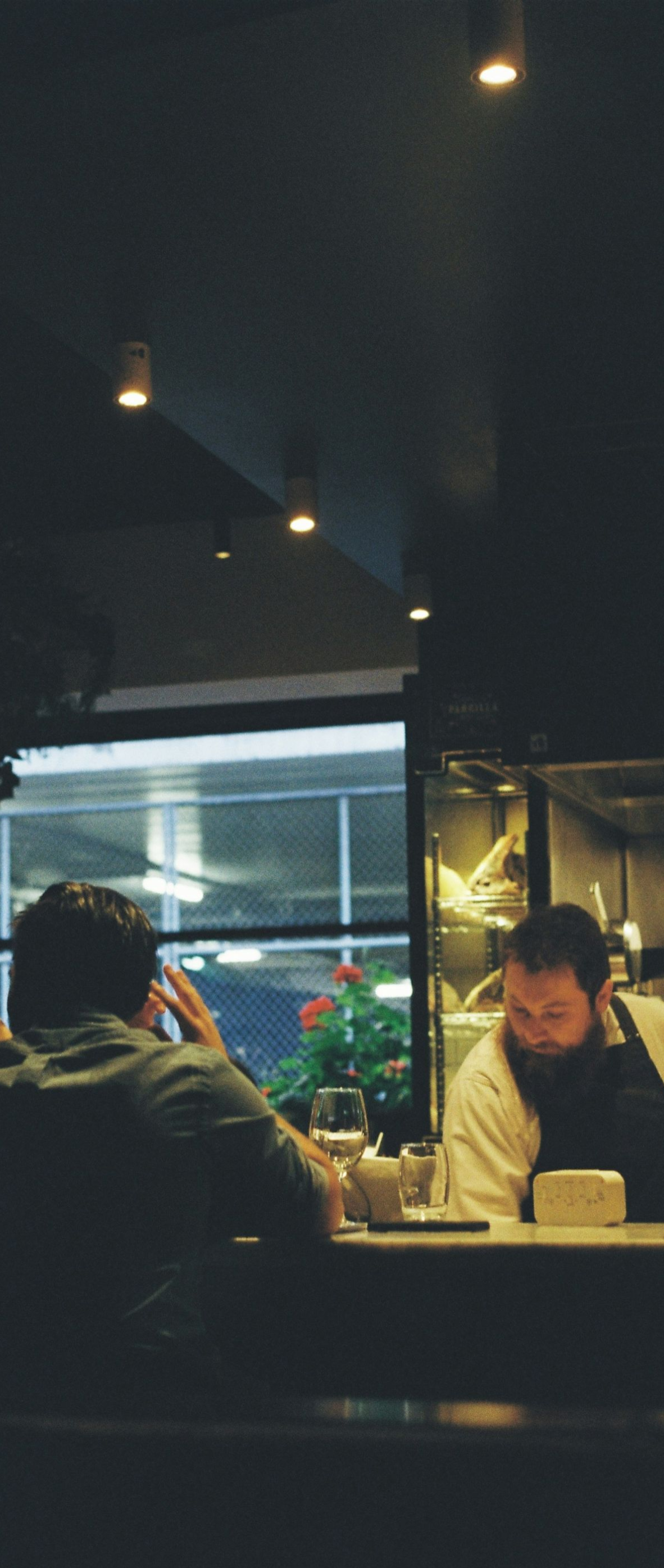 Dim café interior with a person seated at a counter under hanging lights, using a laptop.