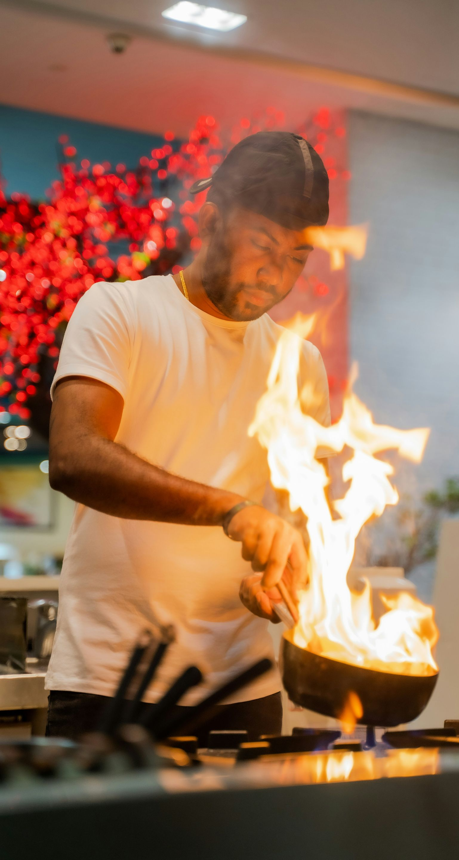 Chef cooking, flames erupt from a pan on a stove in a brightly lit kitchen.