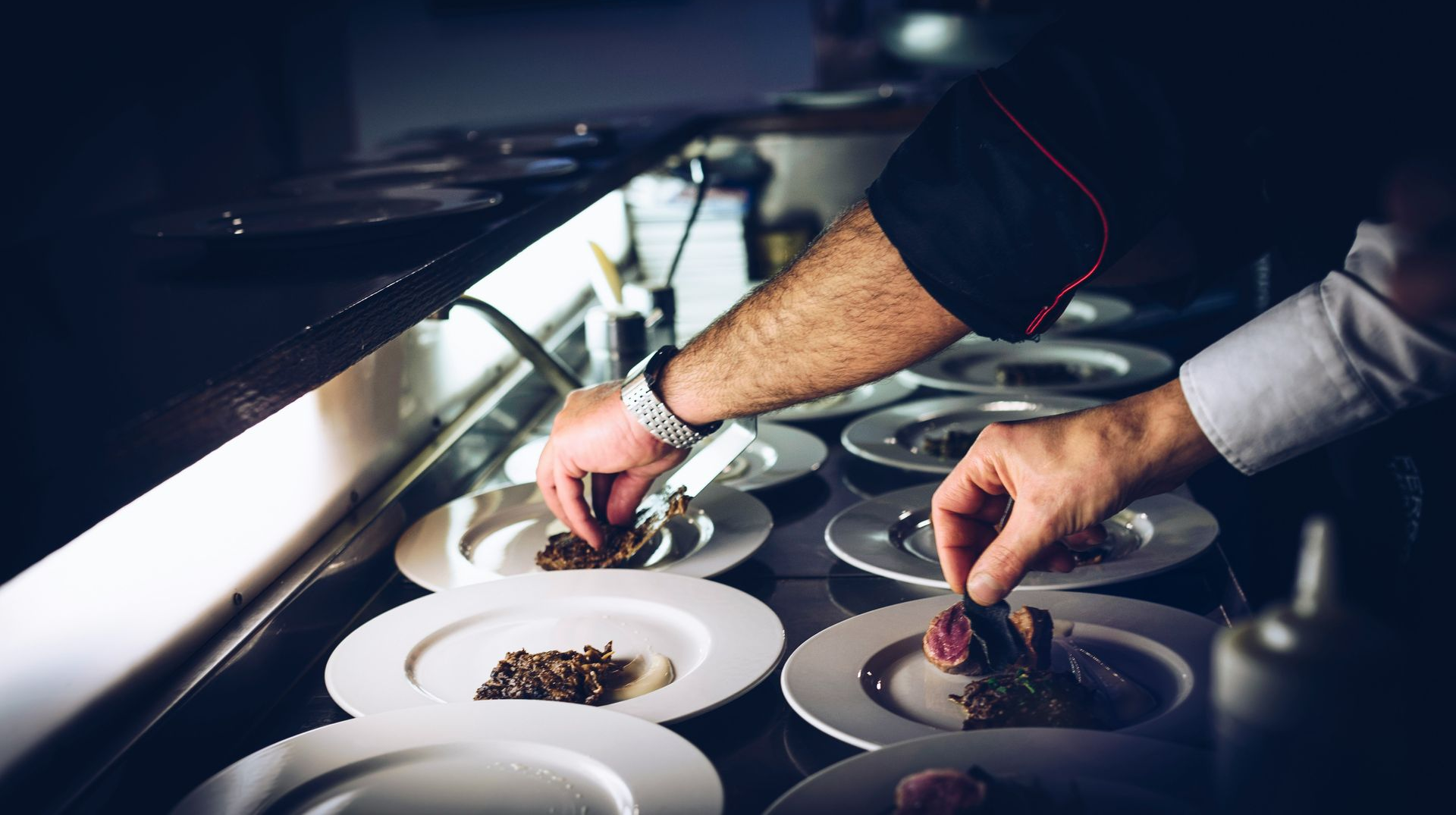 Chef plates food on white plates in a restaurant kitchen.