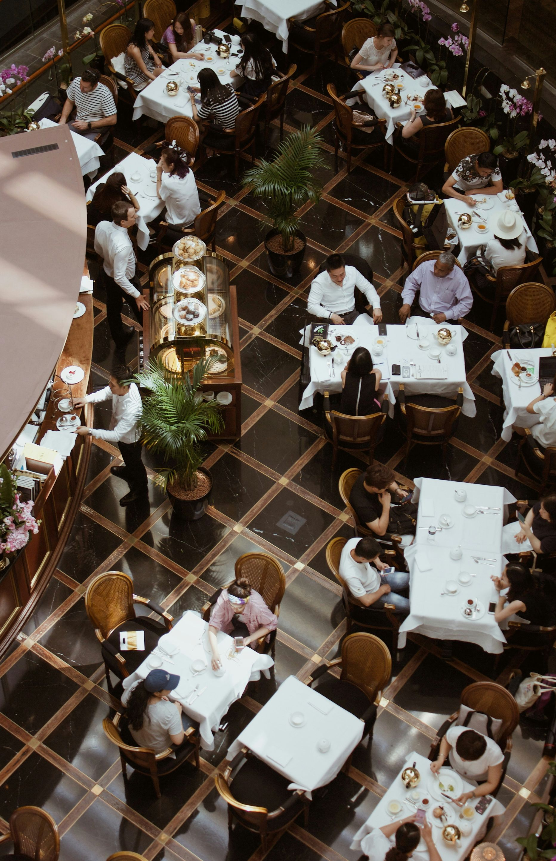 High-angle view of a restaurant. People seated at white-clothed tables, a server tending, dark patterned floors.