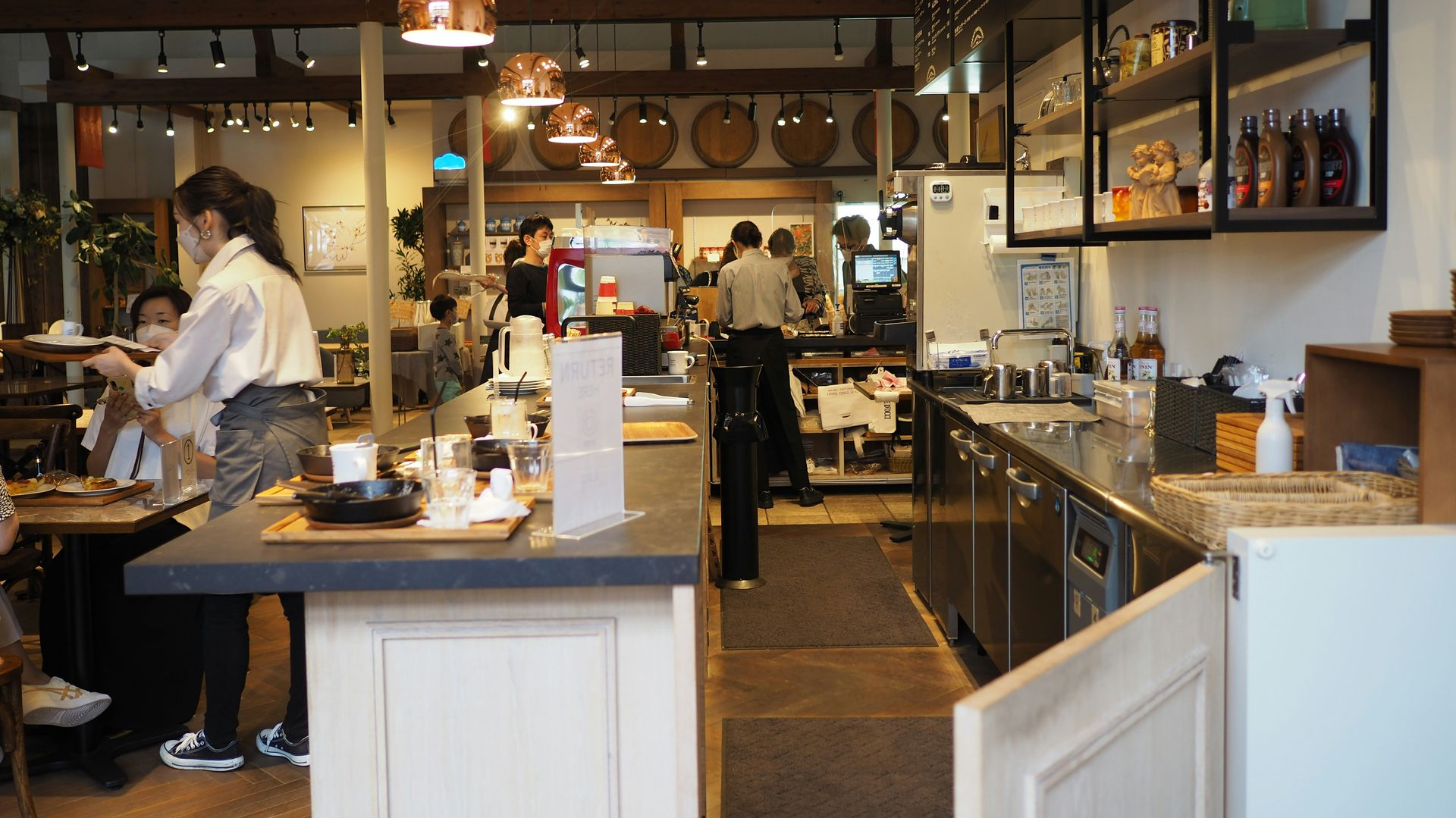 Bright café interior with a counter, shelves, hanging lights, and staff preparing food