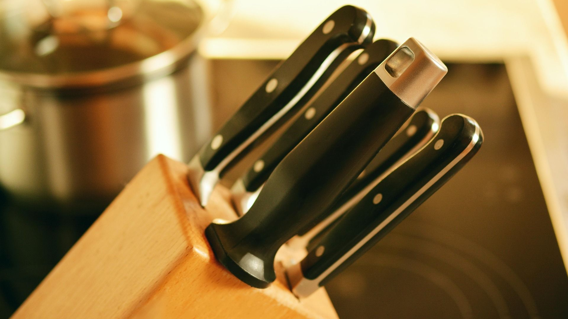 Knives in a wooden block on a stove top, with a pot in the blurred background.