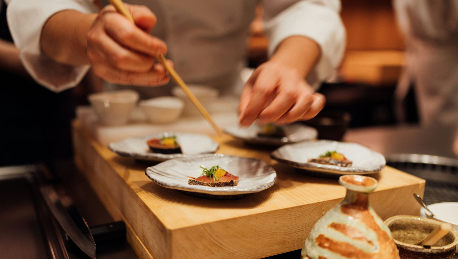 Chef arranging small dishes with chopsticks in a restaurant setting.