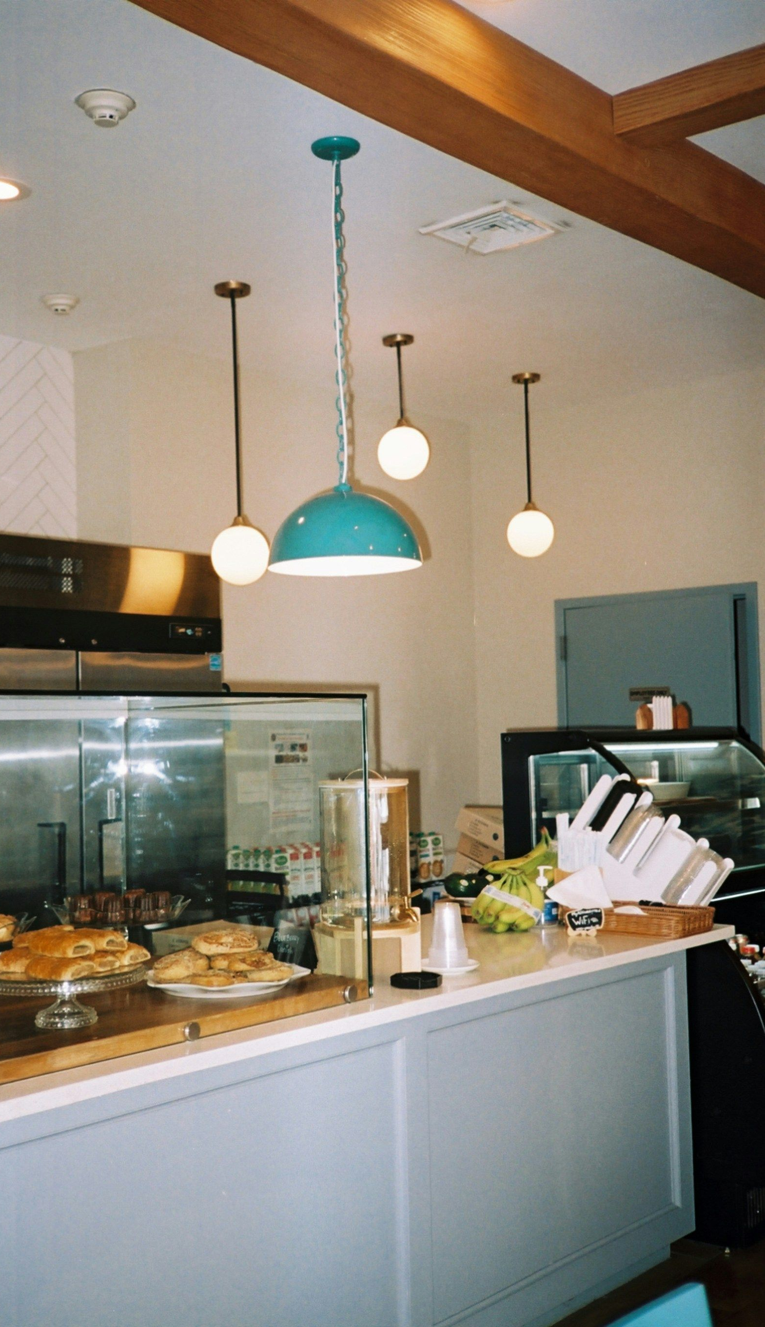 Cafe interior with turquoise pendant lights hanging above a white counter with food and a glass display case.