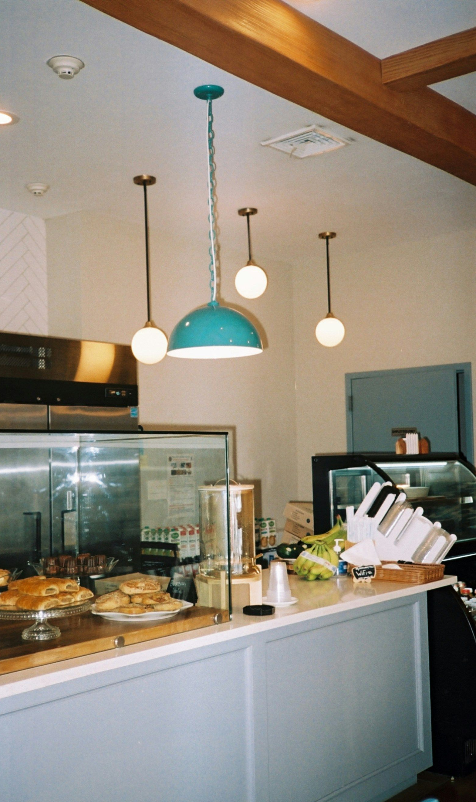 A cafe interior with turquoise pendant lights and counter, food displays, and a glass-door refrigerator.
