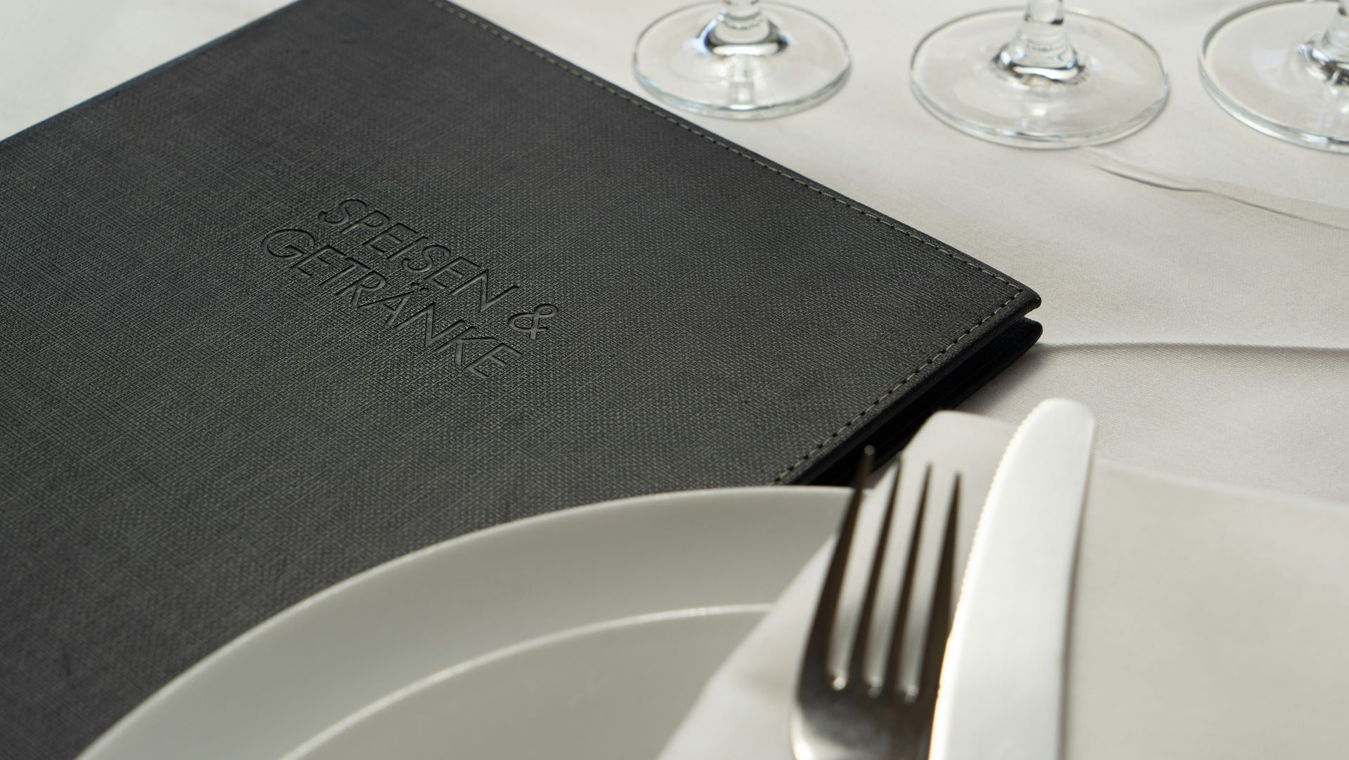 Place setting with plate, fork, knife, napkin, and menu on a table.