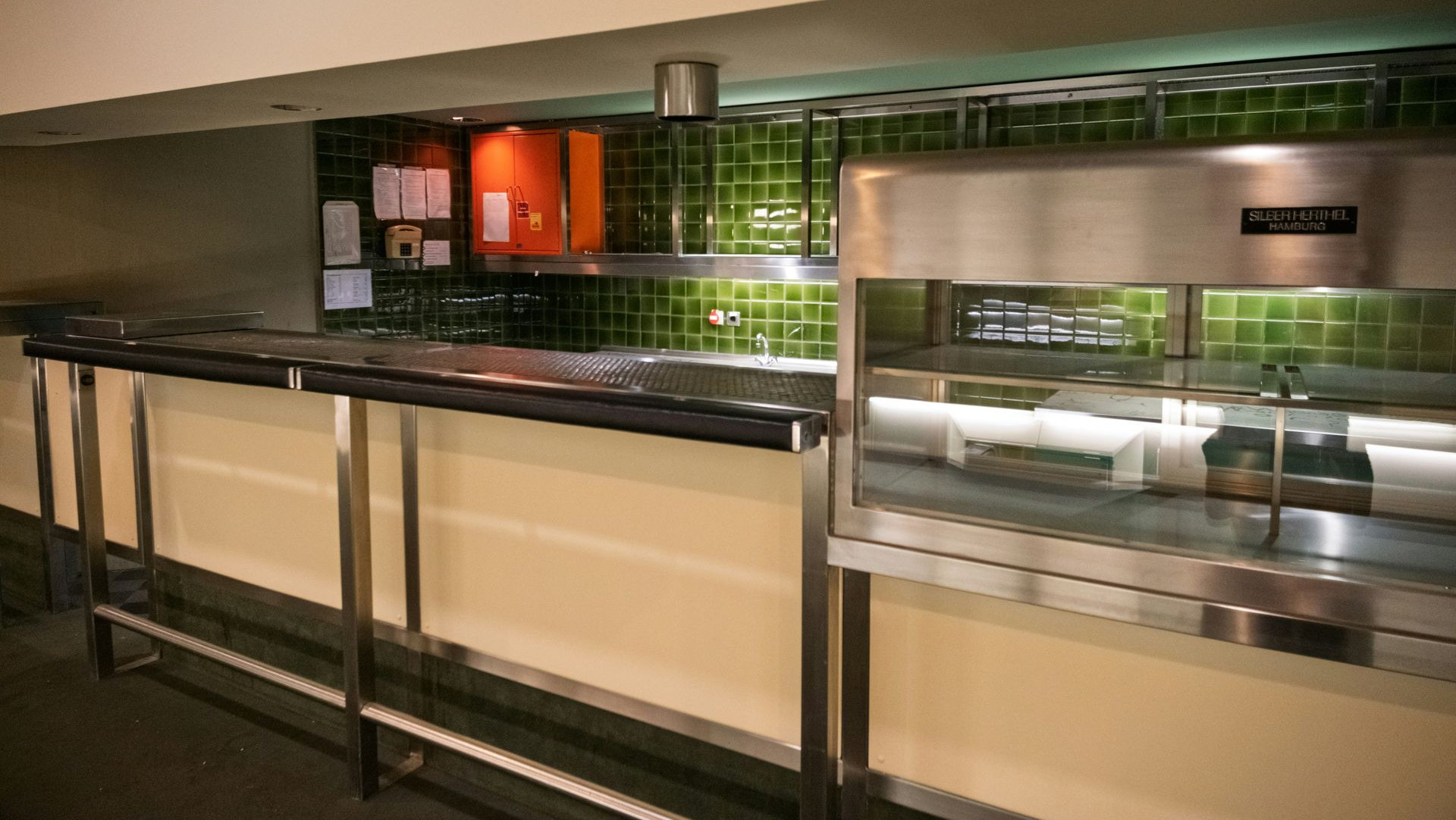 Stainless steel service counter with green tiled backsplash and warm accent lighting in a modern interior setting.