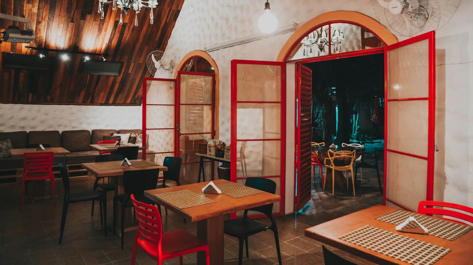 Interior of a cafe with wooden tables, red and black chairs, and arched doorways leading outside.