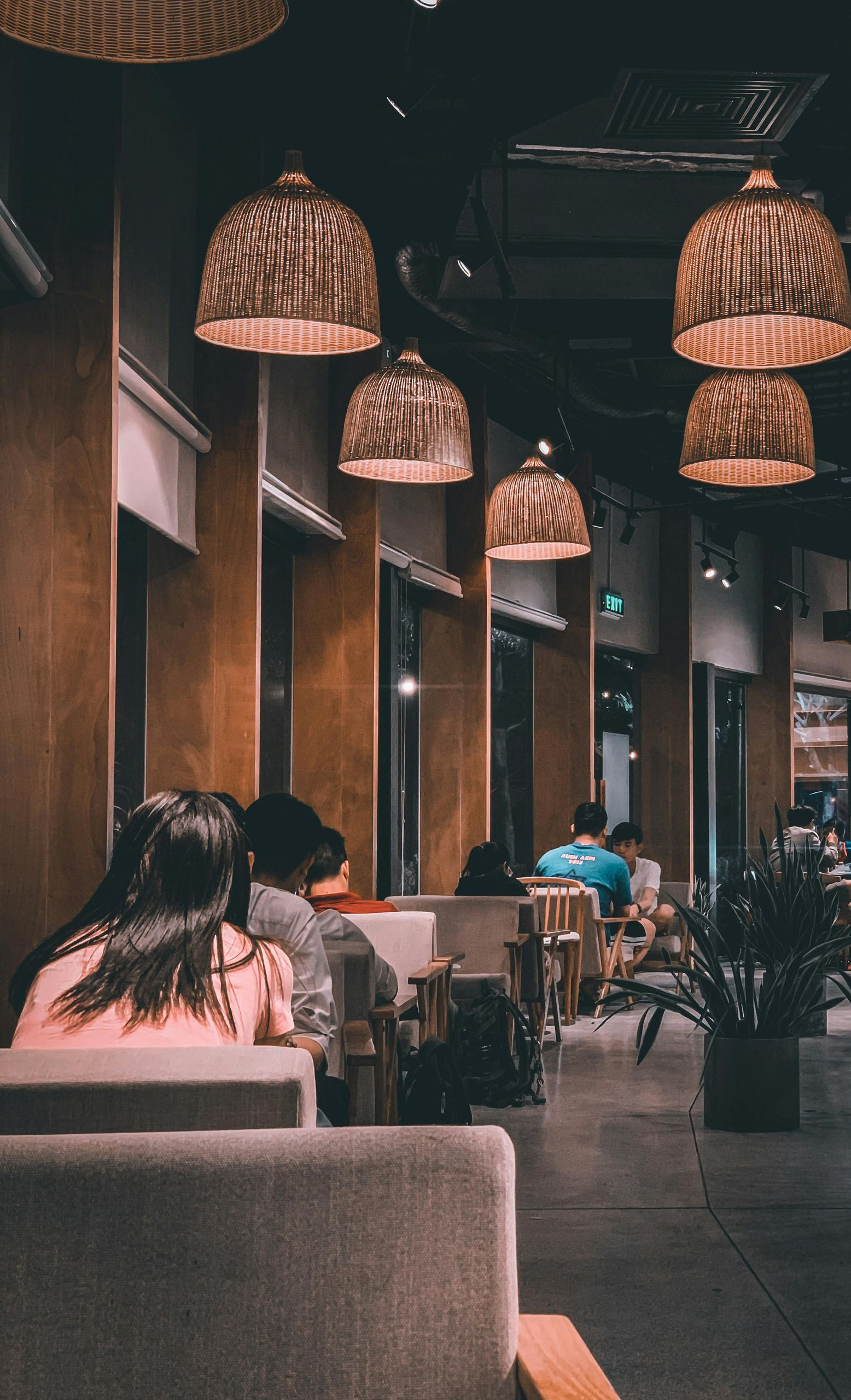 Dimly lit cafe interior with woven pendant lights, people seated at tables.