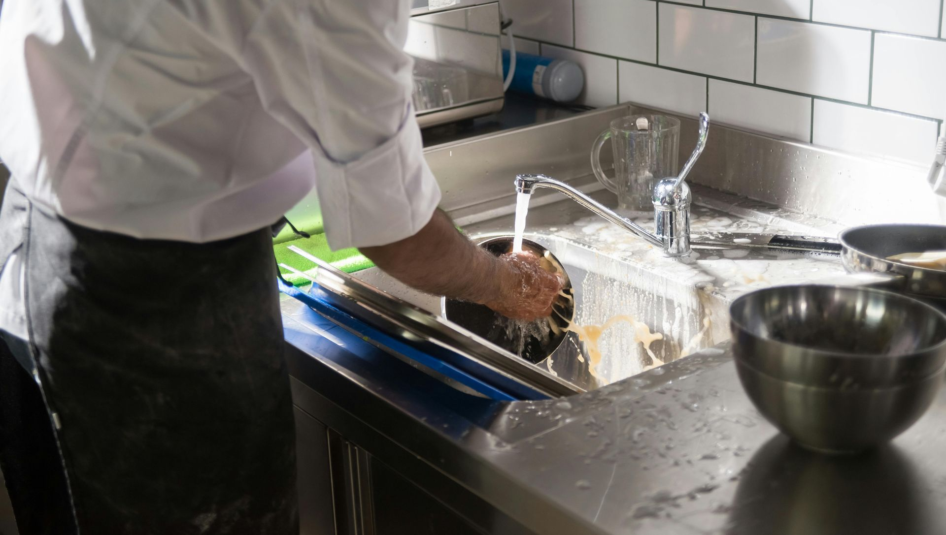 Chef washing dishes in a stainless steel sink, kitchen setting.