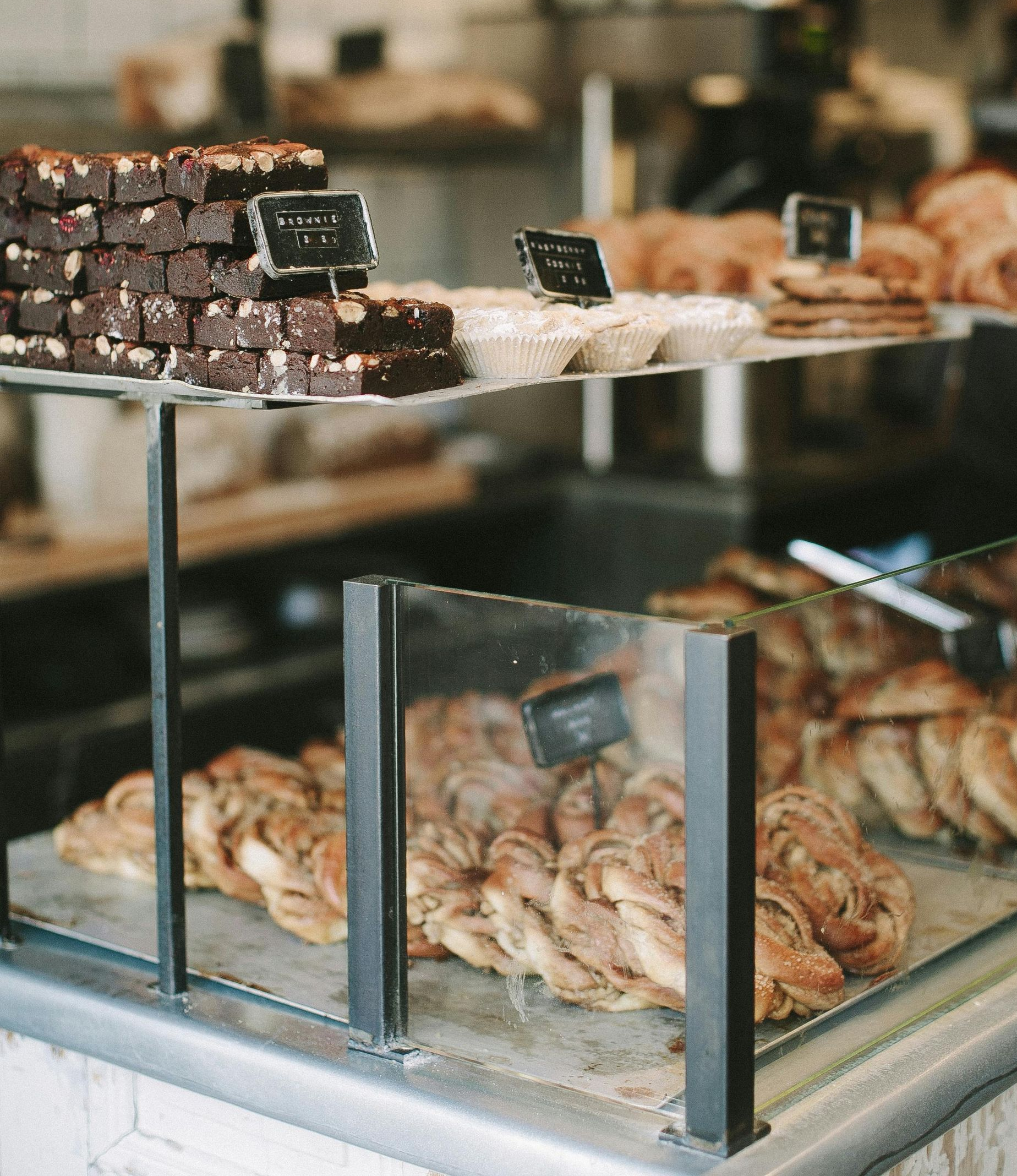 A bakery display case filled with rows of dark chocolate brownies and light-colored braided pastries on metal trays.