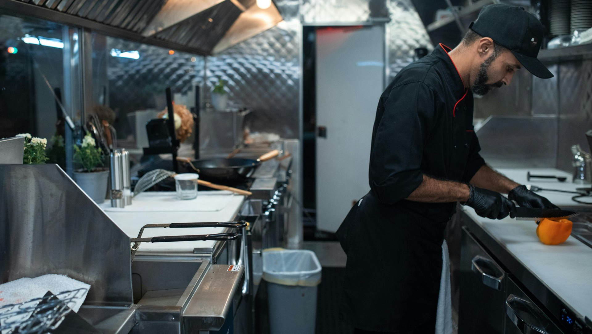Chef in black uniform preparing food in a commercial kitchen with stainless steel surfaces and a bright yellow pepper.