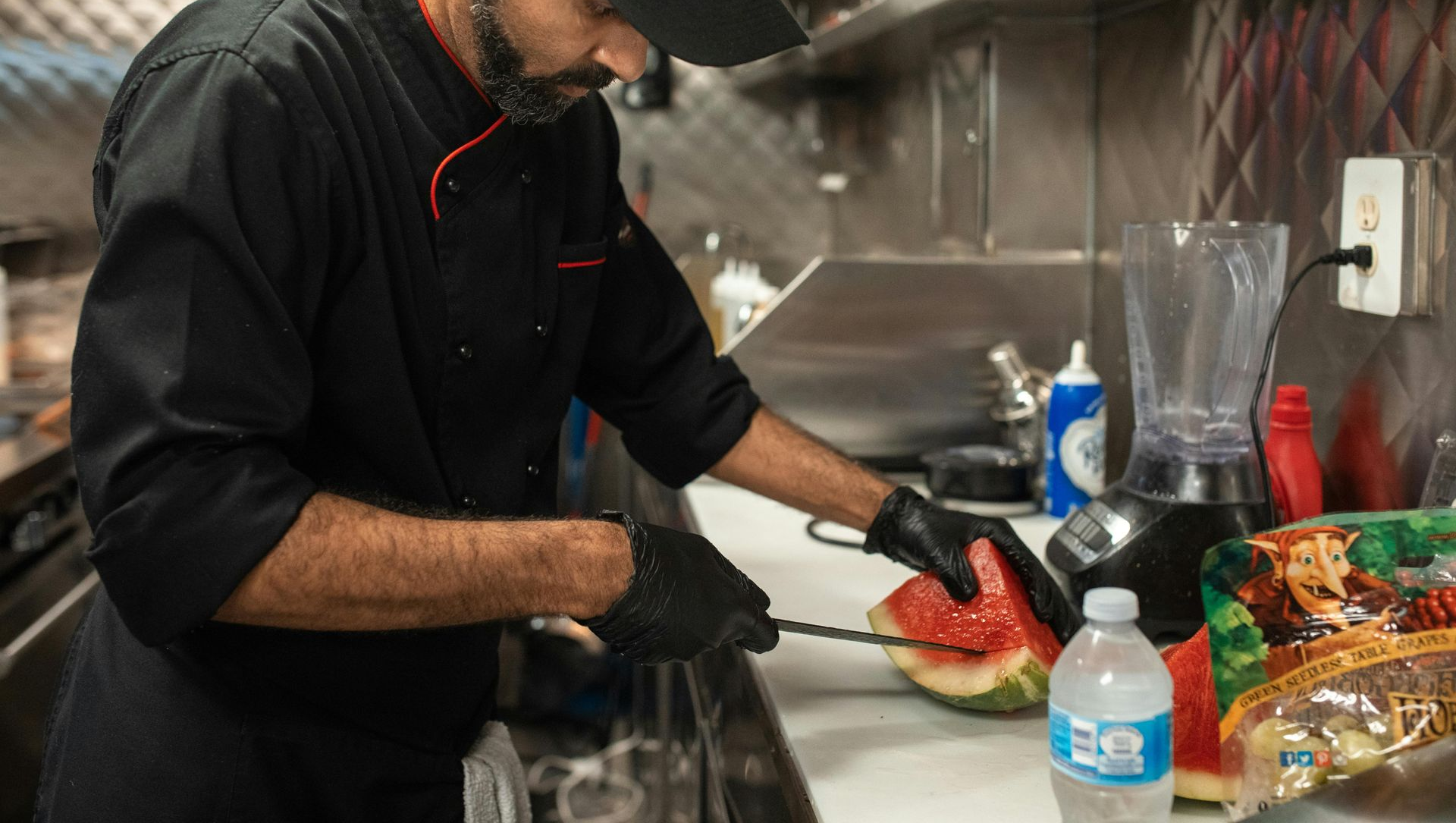 Chef in black uniform cutting watermelon in a food truck kitchen.