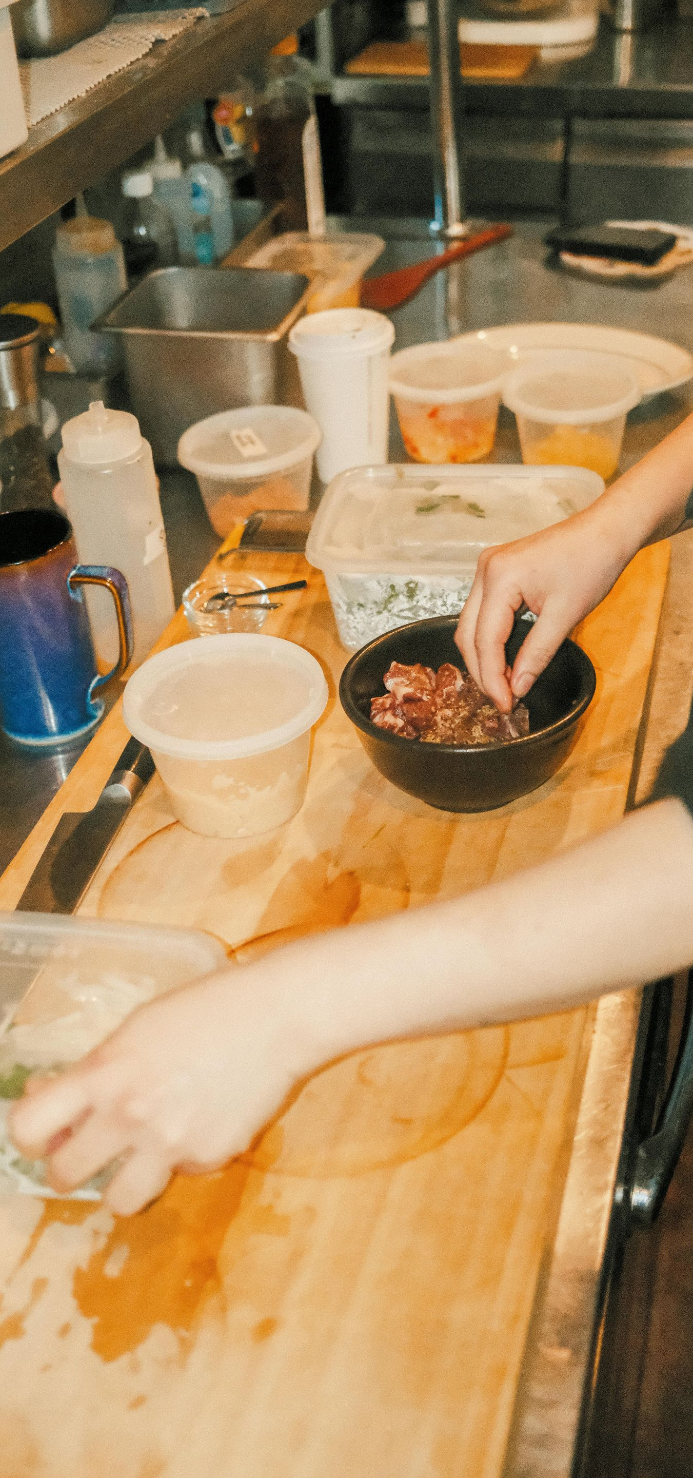 A person wearing a black shirt prepares food in a kitchen, mixing ingredients in a bowl on a wooden countertop.