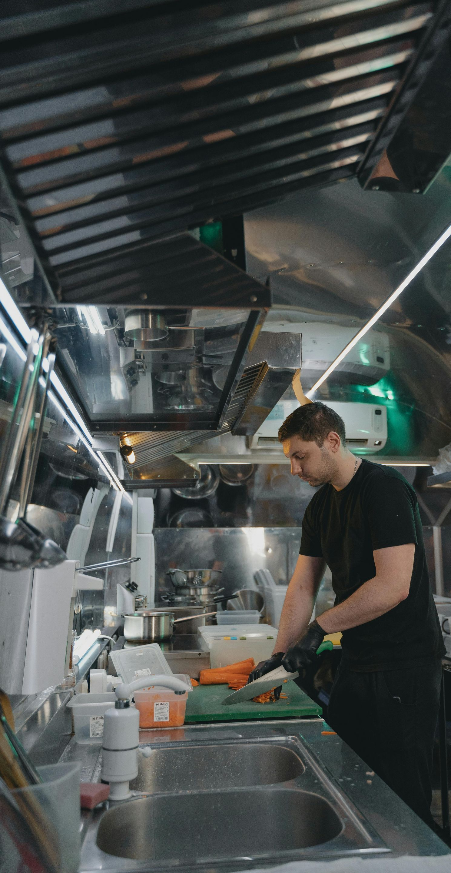 Chef in black uniform slicing food at a kitchen counter with stainless steel appliances.