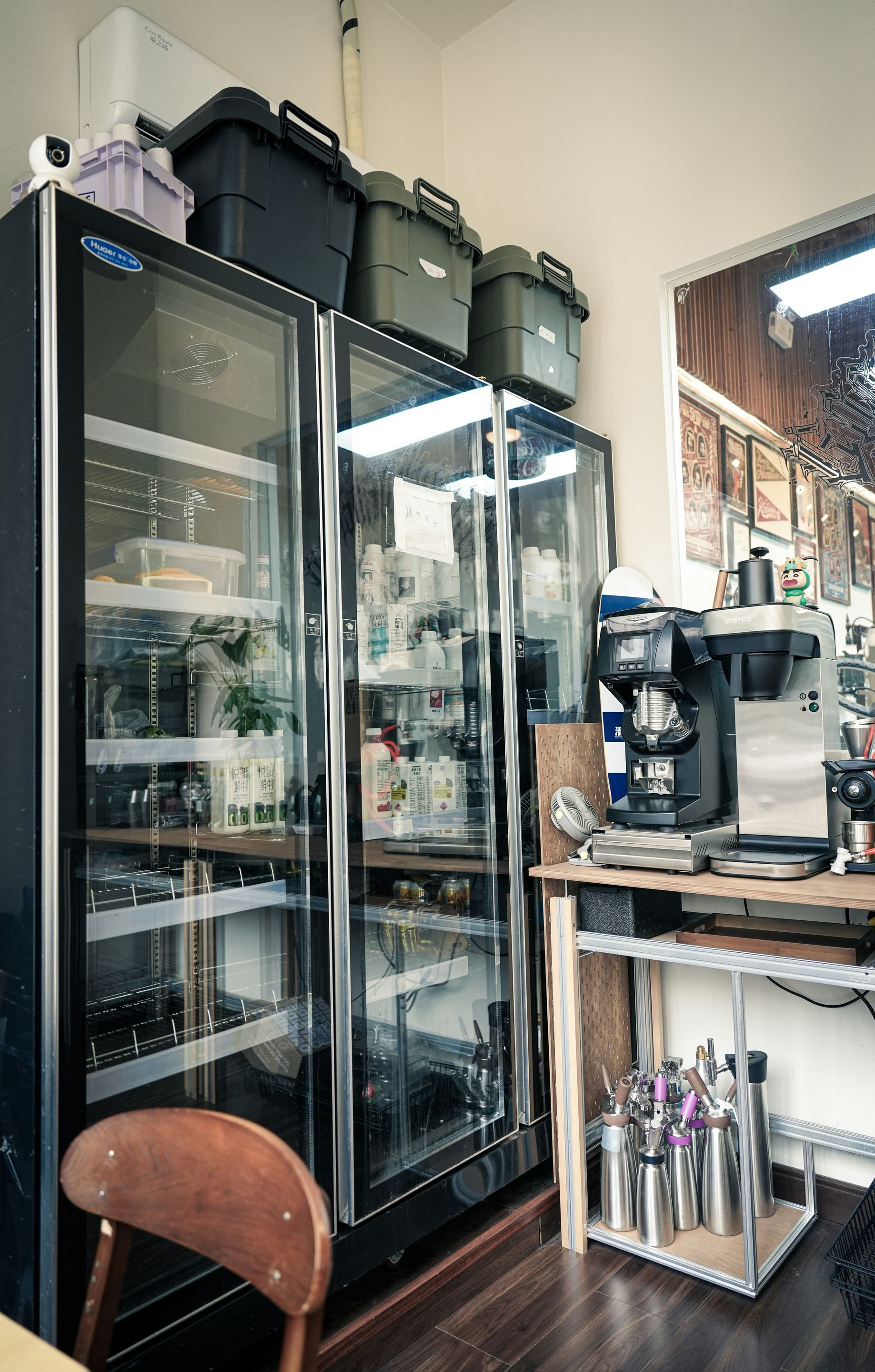 Refrigerators and coffee maker in a cafe. Black storage containers are stacked on top of refrigerators.