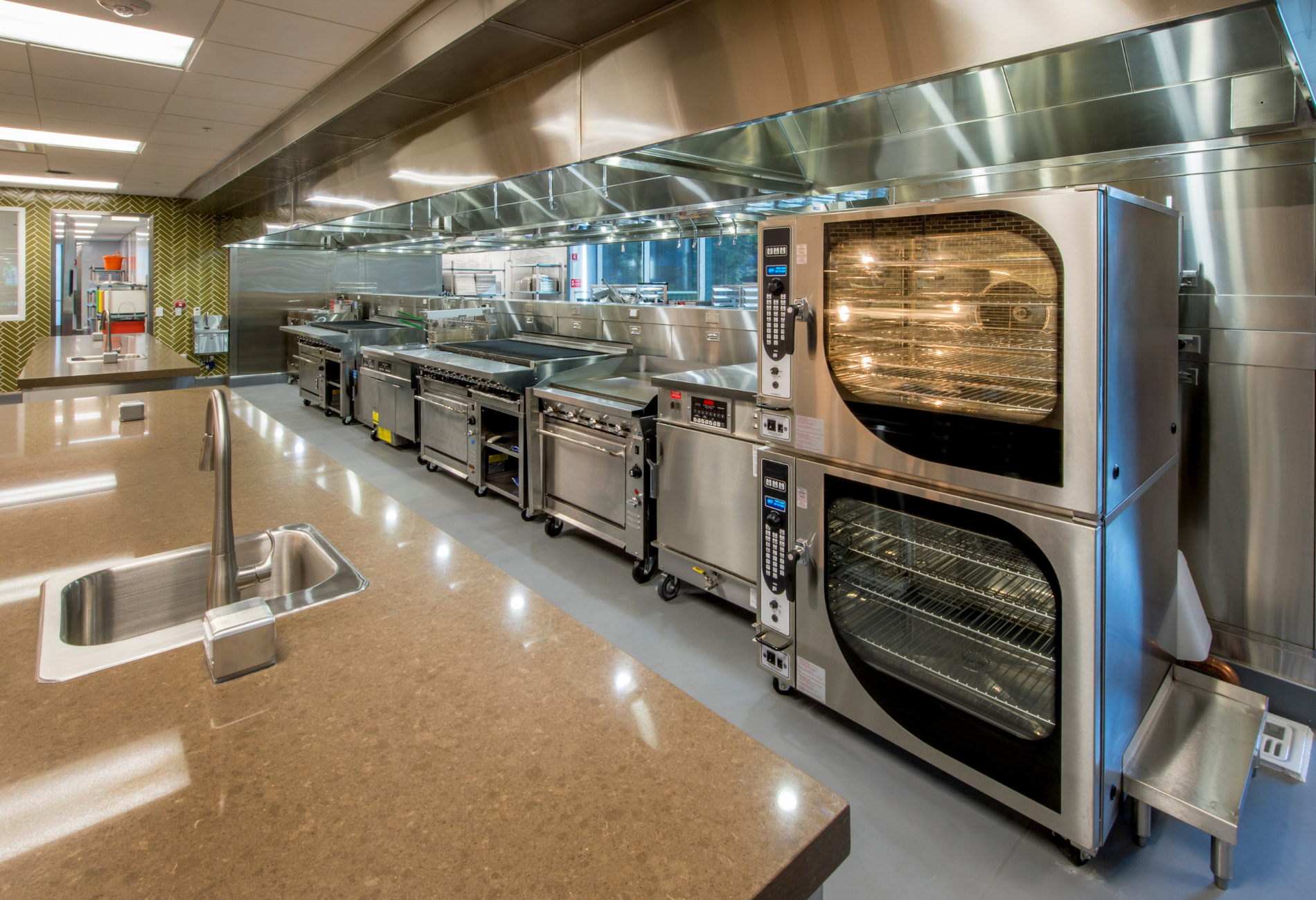Commercial kitchen with stainless steel appliances and ventilation hoods, countertop sink.