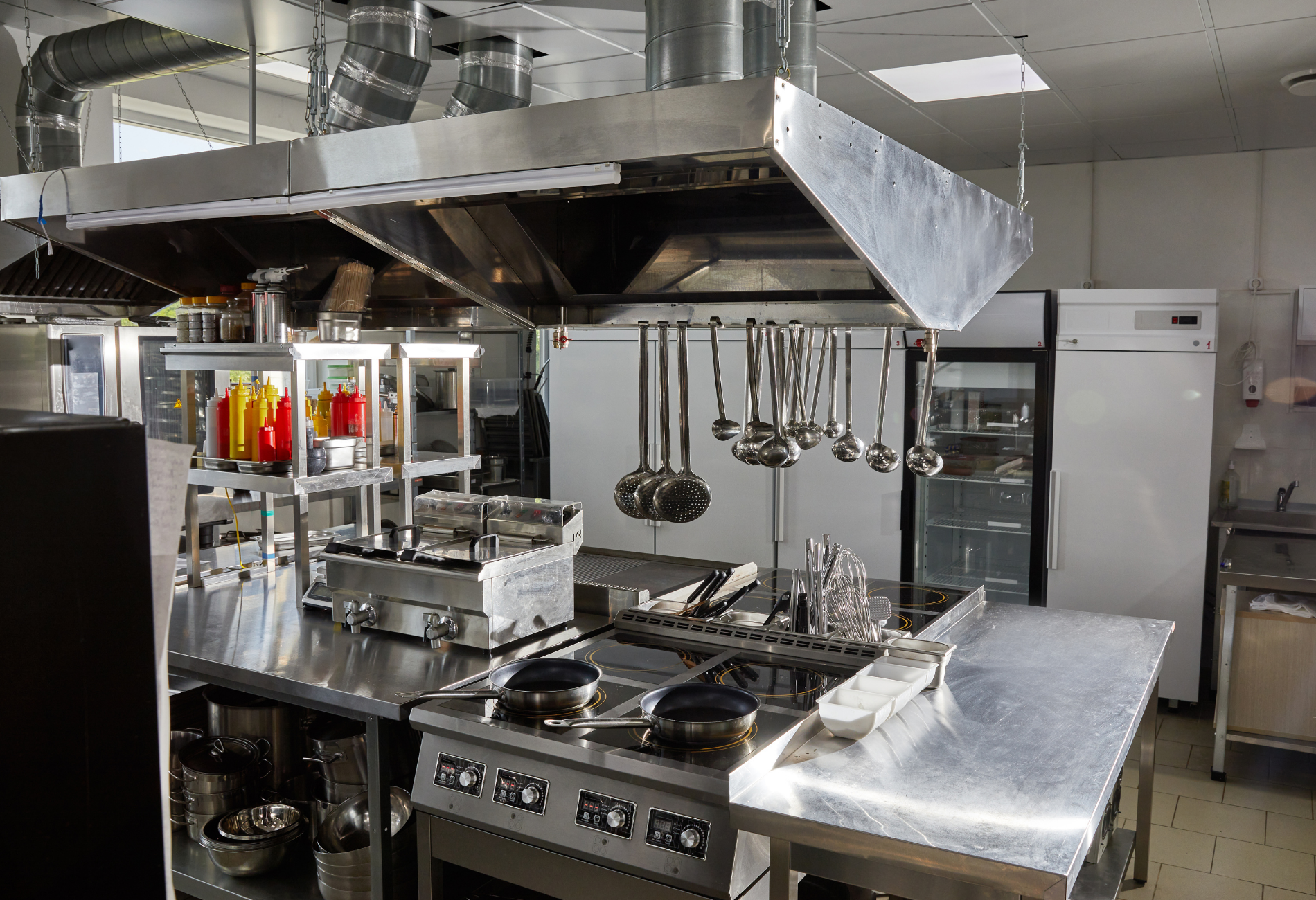 Commercial kitchen with stainless steel appliances, vent hood, and utensils.