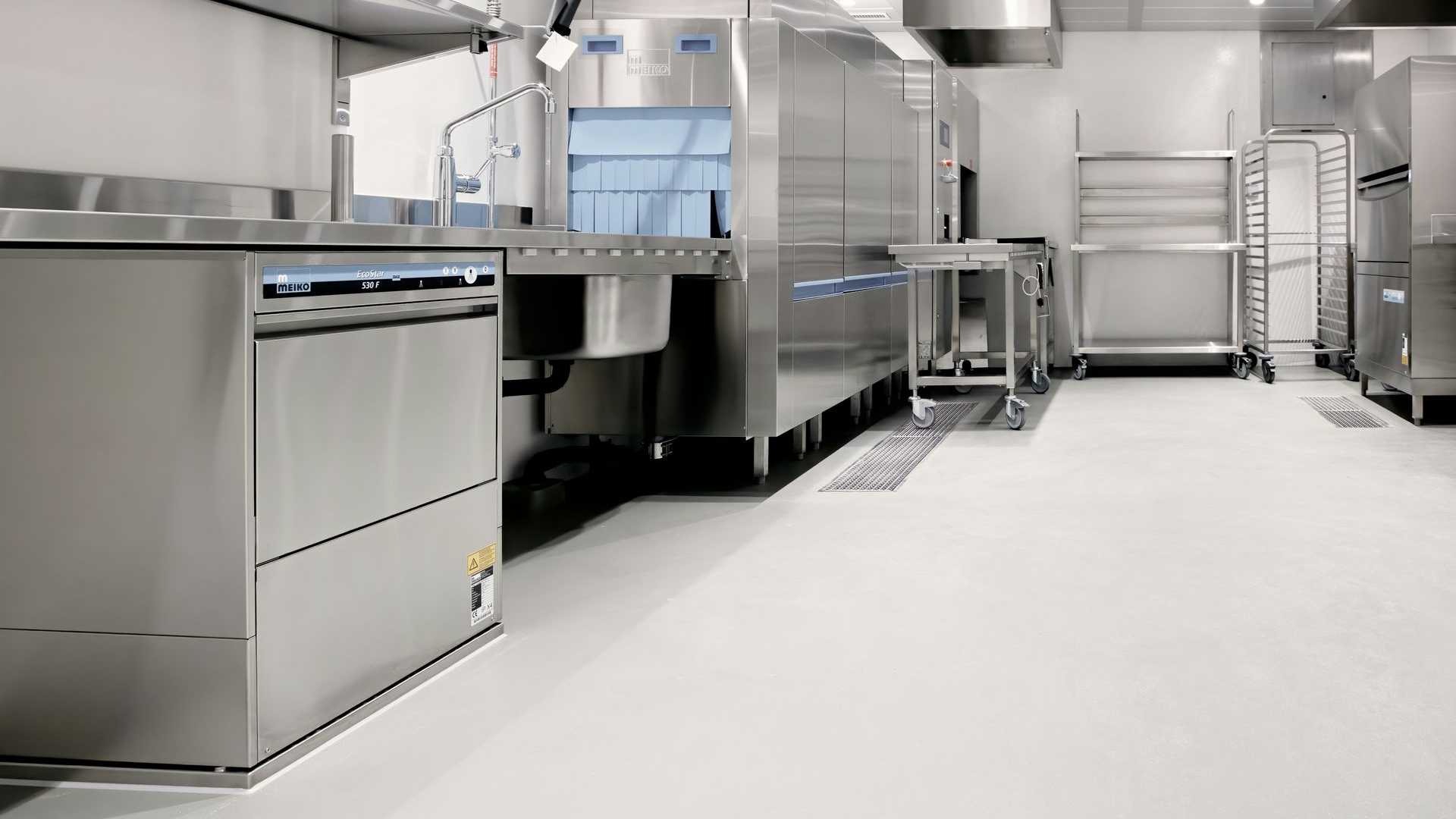 Stainless steel commercial kitchen with industrial dishwasher, sink, and storage shelving.