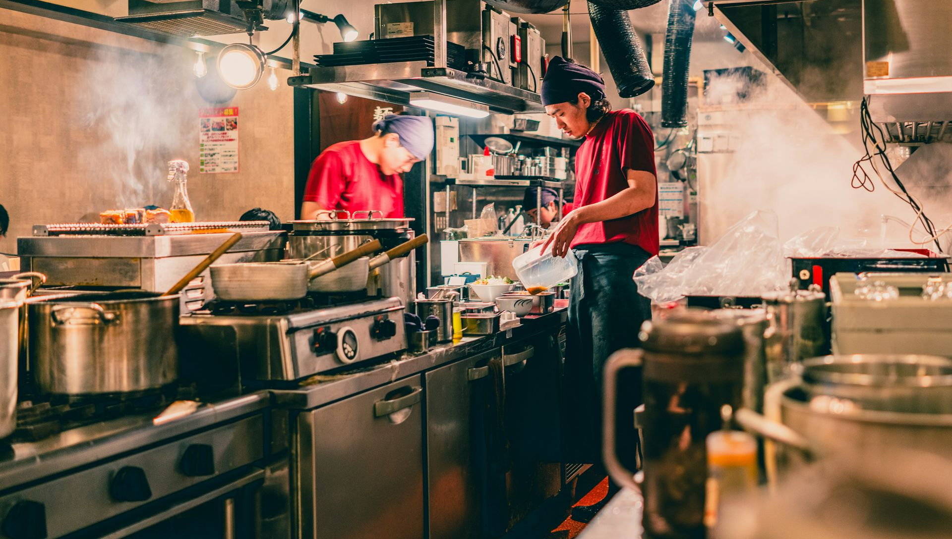 Busy restaurant kitchen with two chefs cooking amid steam and stainless steel equipment