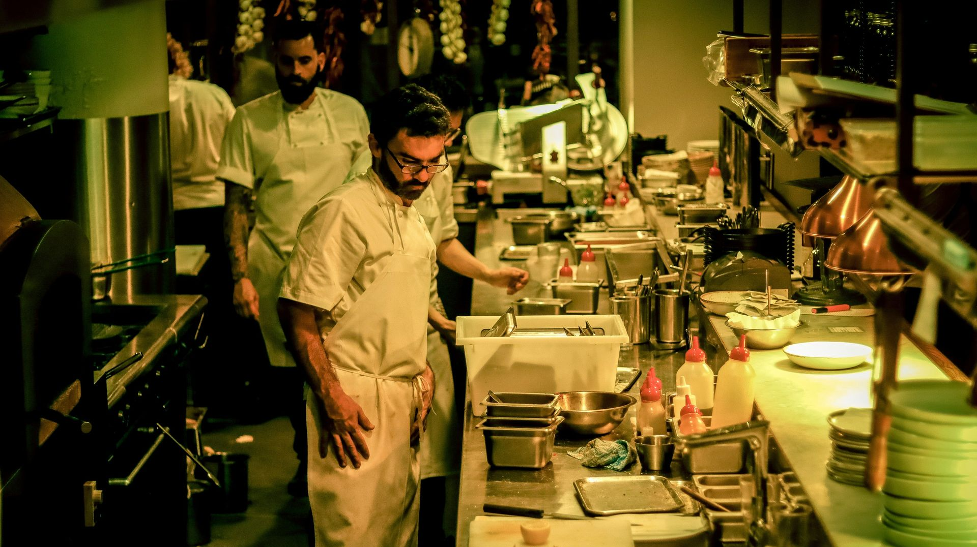 Chefs working in a busy restaurant kitchen with stainless steel counters and stacked green plates