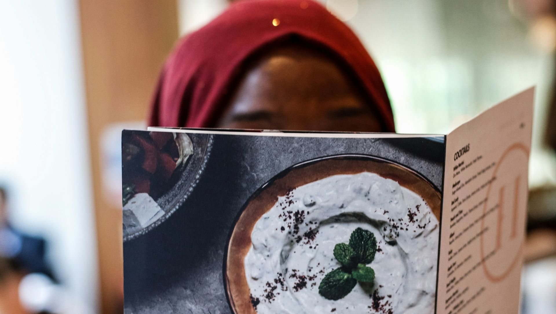 Woman in red headscarf looking at menu with food picture.