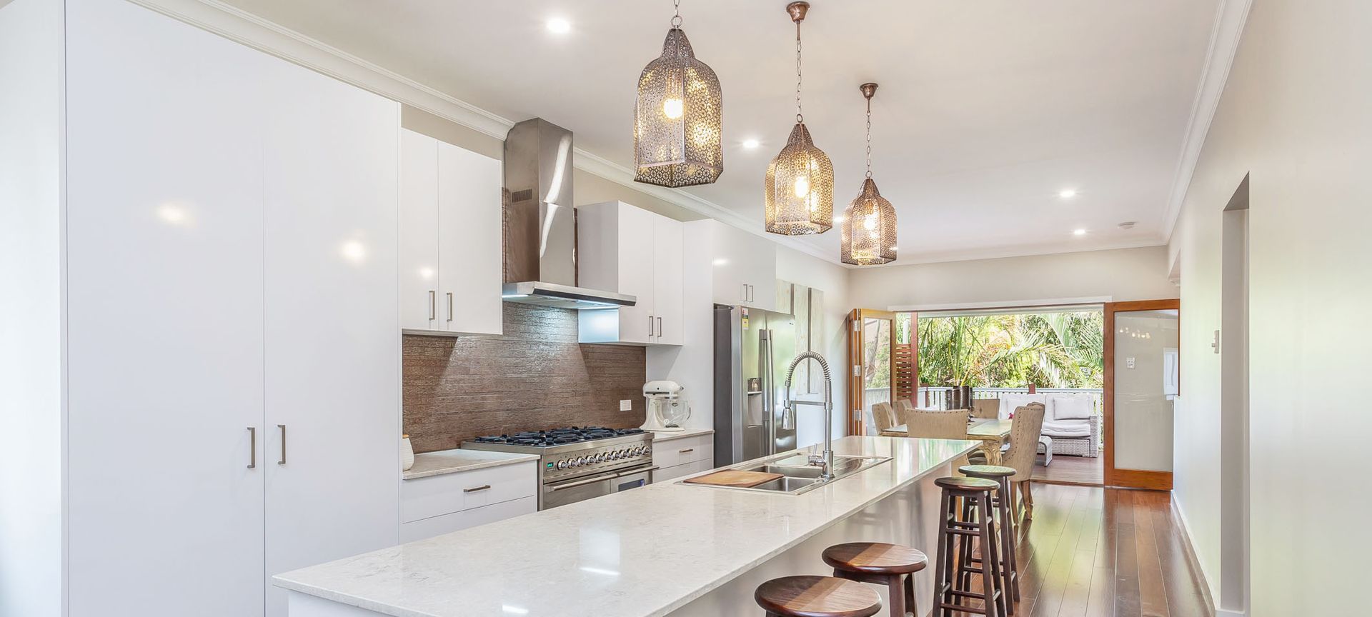 A modern kitchen with white cabinetry, a long island with stools, and pendant lights.