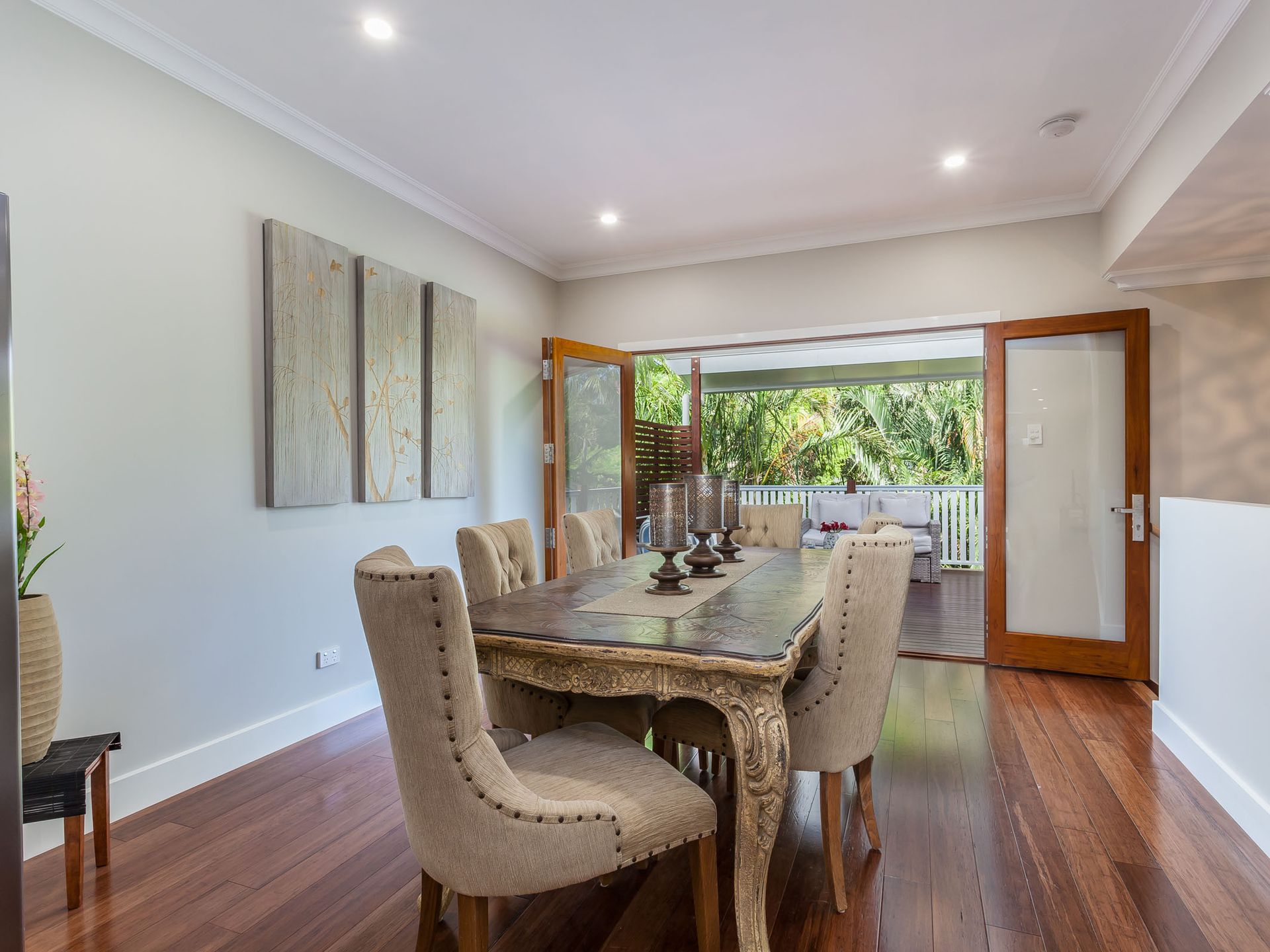 Dining room with wooden floors, table, and chairs; French doors open to a patio. Artwork hangs on the wall.