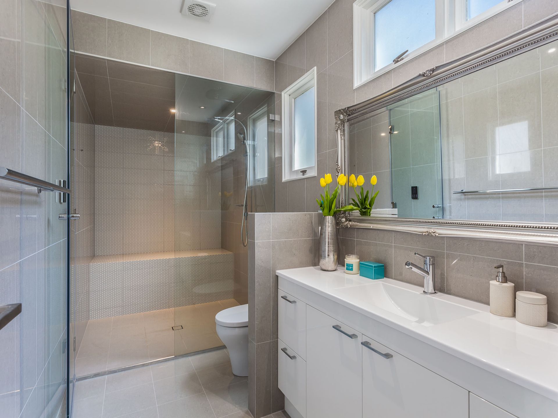 Modern bathroom with a glass shower, white vanity, and large mirror; neutral gray and white color scheme.