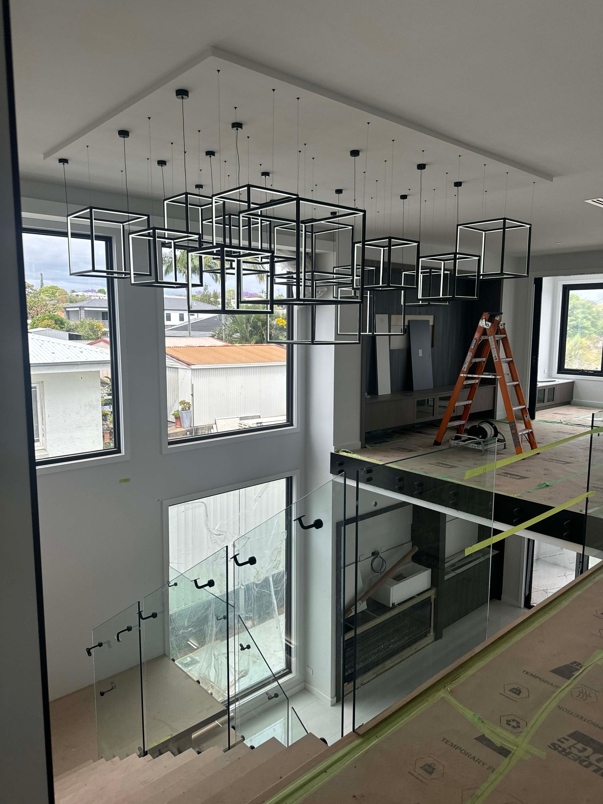 A high-ceilinged modern room with a large abstract chandelier hanging above a kitchen area under construction.
