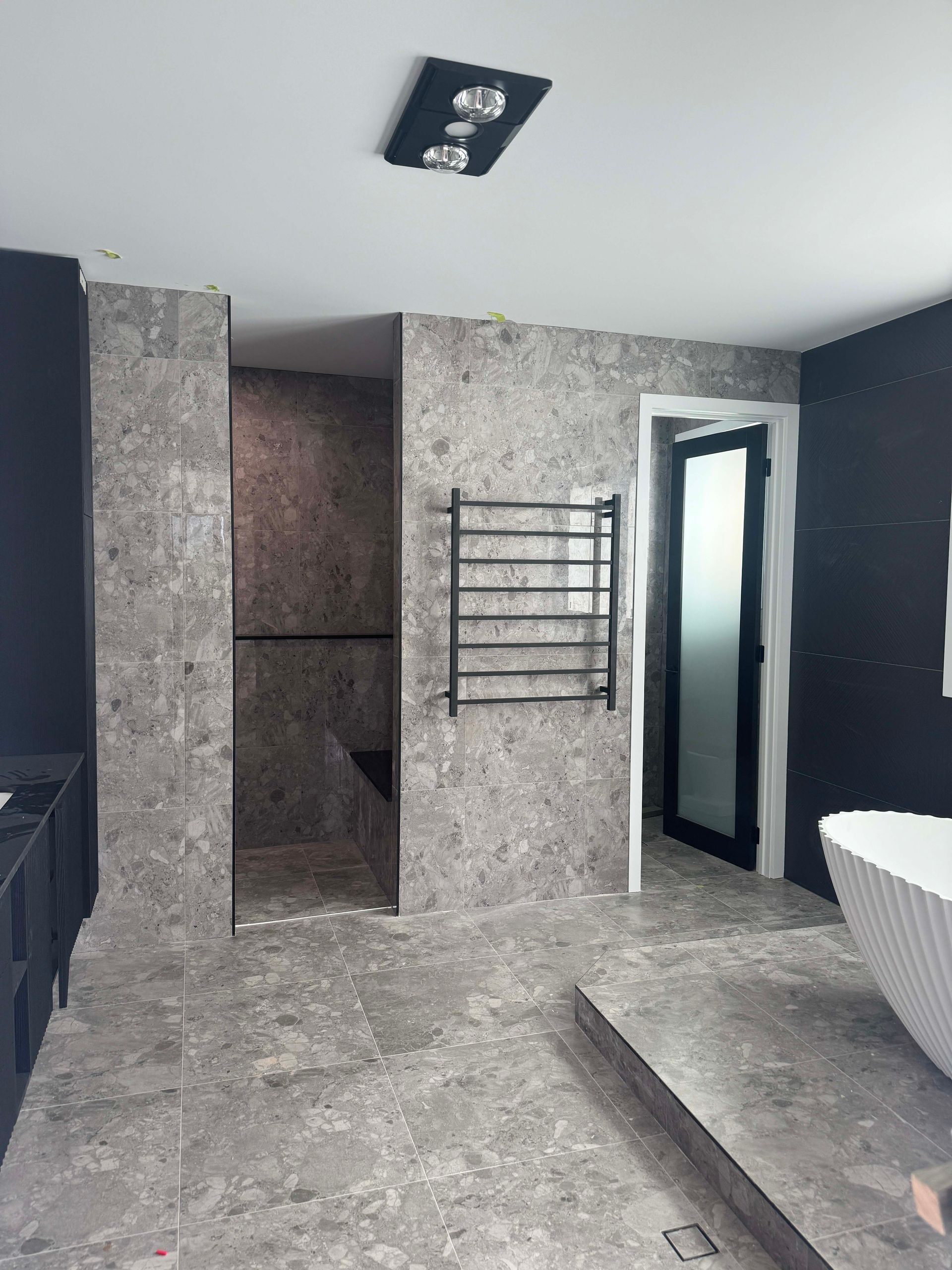 A modern bathroom under construction with gray stone tiles on the floor and walls. 