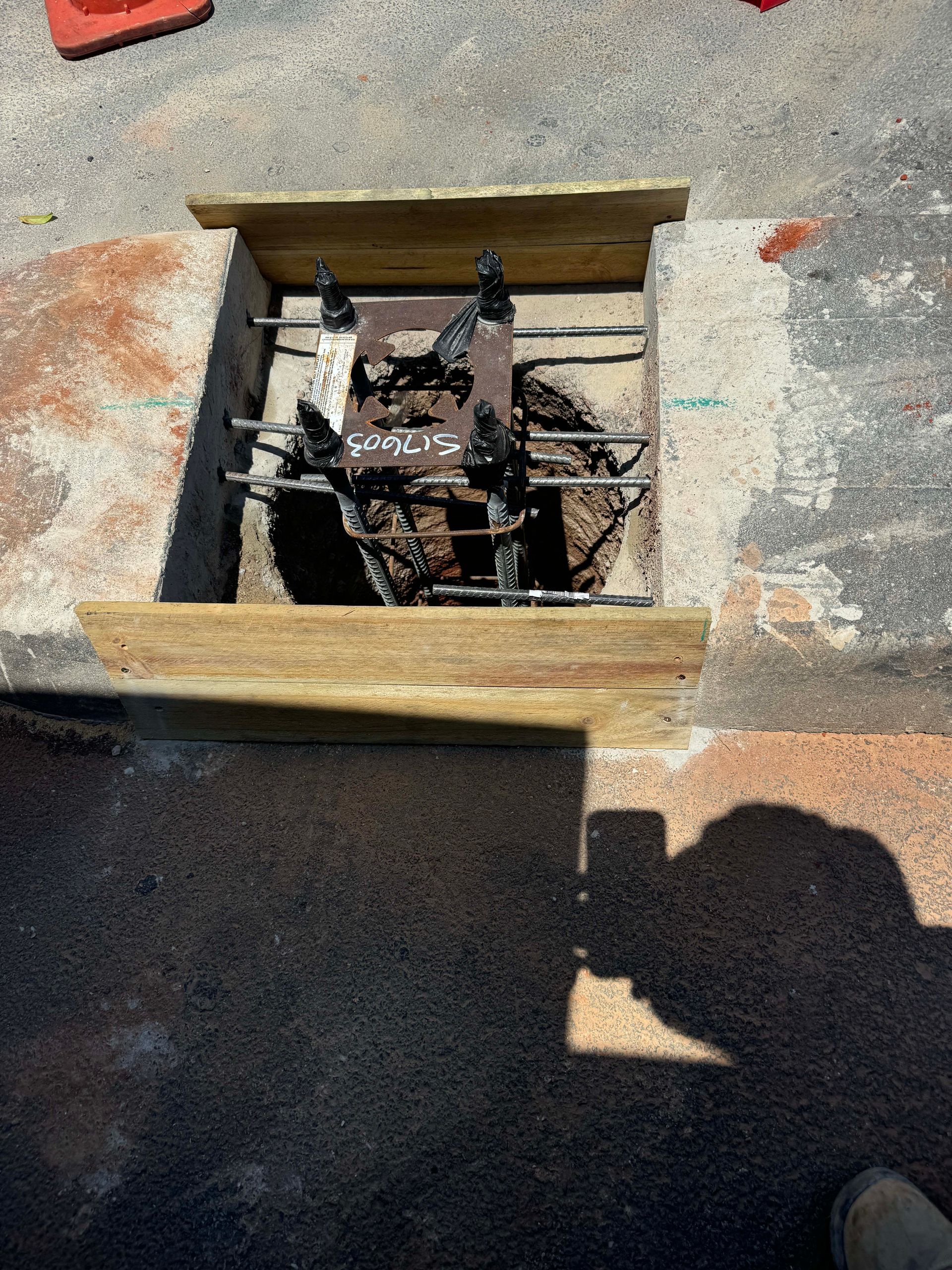 A square cutout in pavement, reinforced with metal, surrounded by wooden framing.