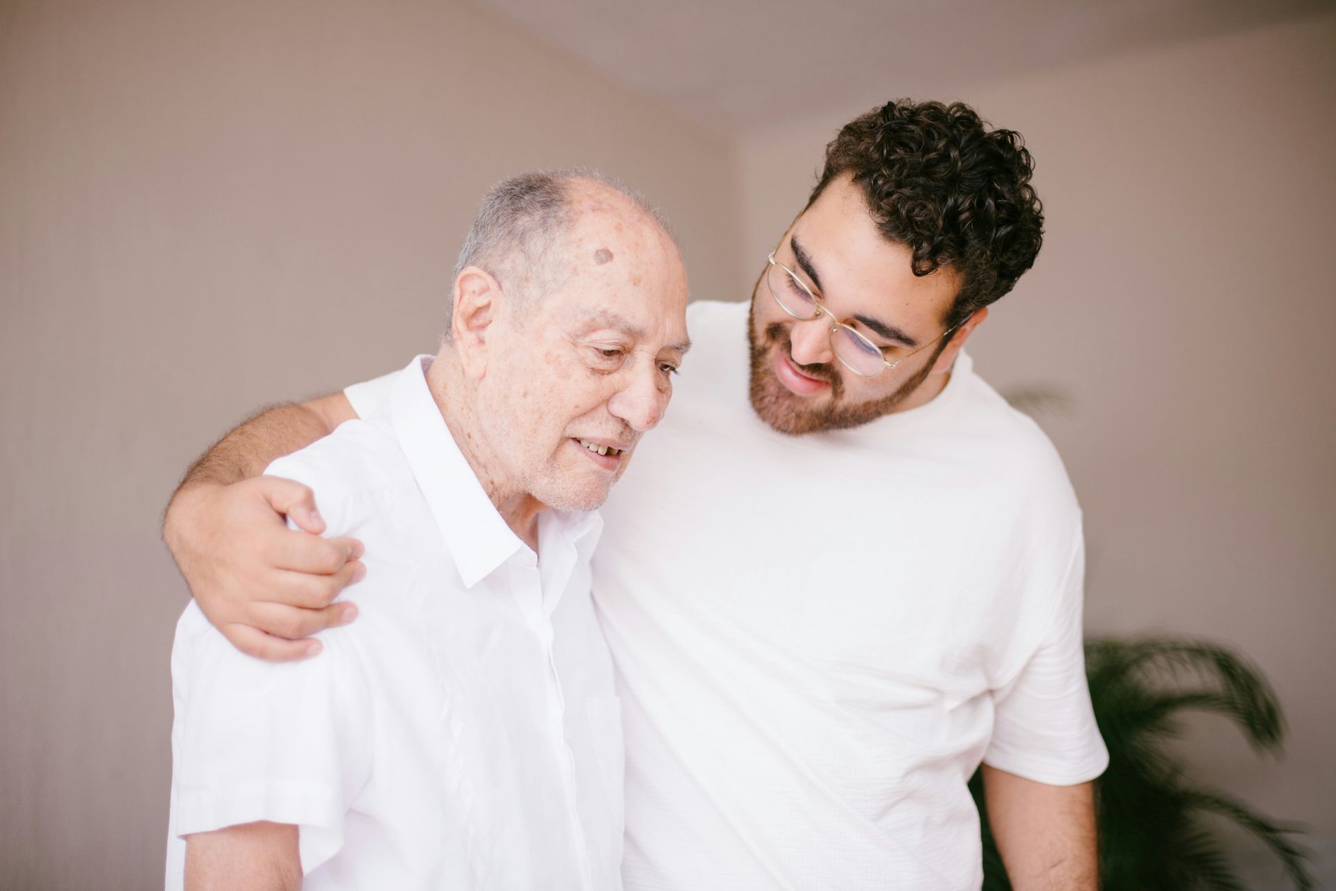 Younger person with arm around older person, smiling, indoor setting, supportive gesture.