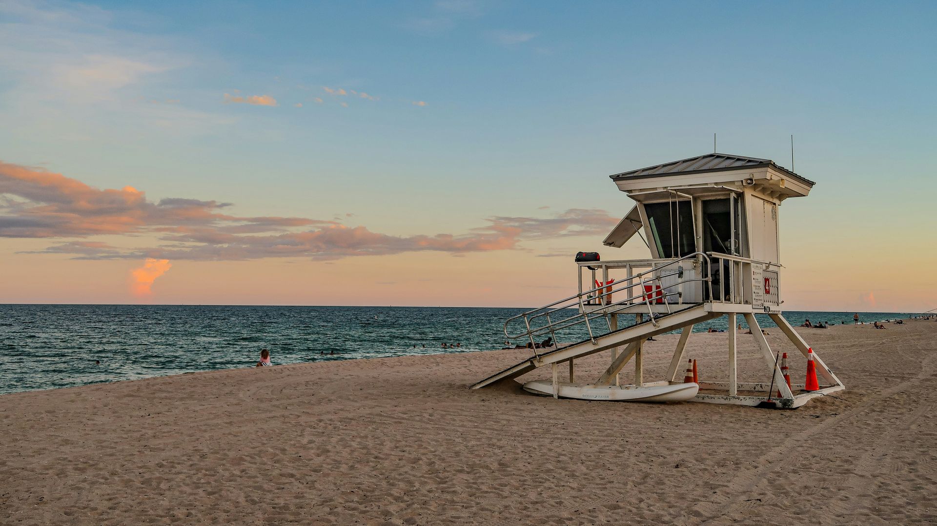 Lifeguard stand on a sandy beach at sunset, ocean waves in the background, pastel sky.