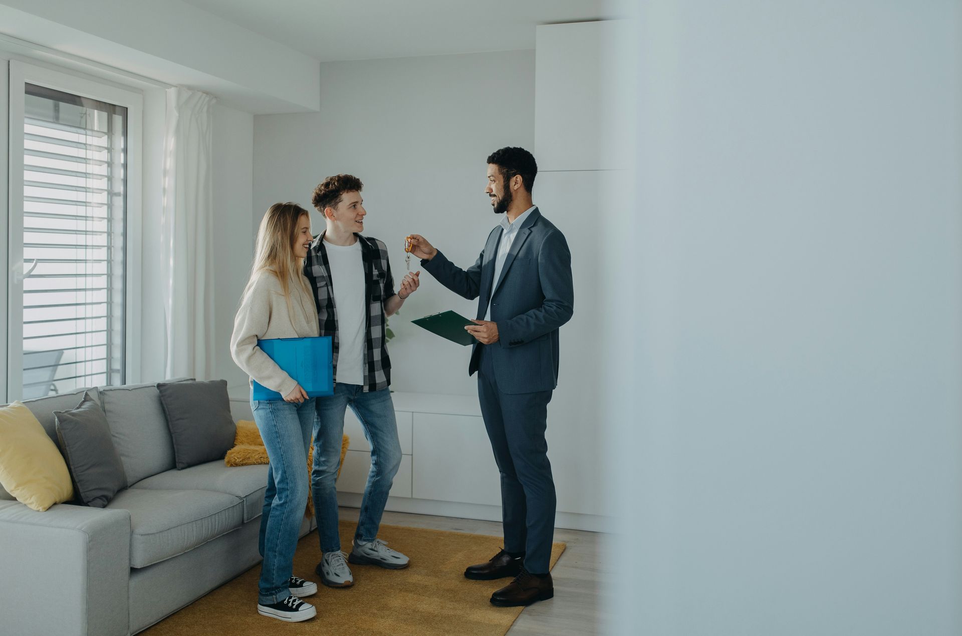 Real estate agent handing keys to a couple in a bright, furnished apartment.