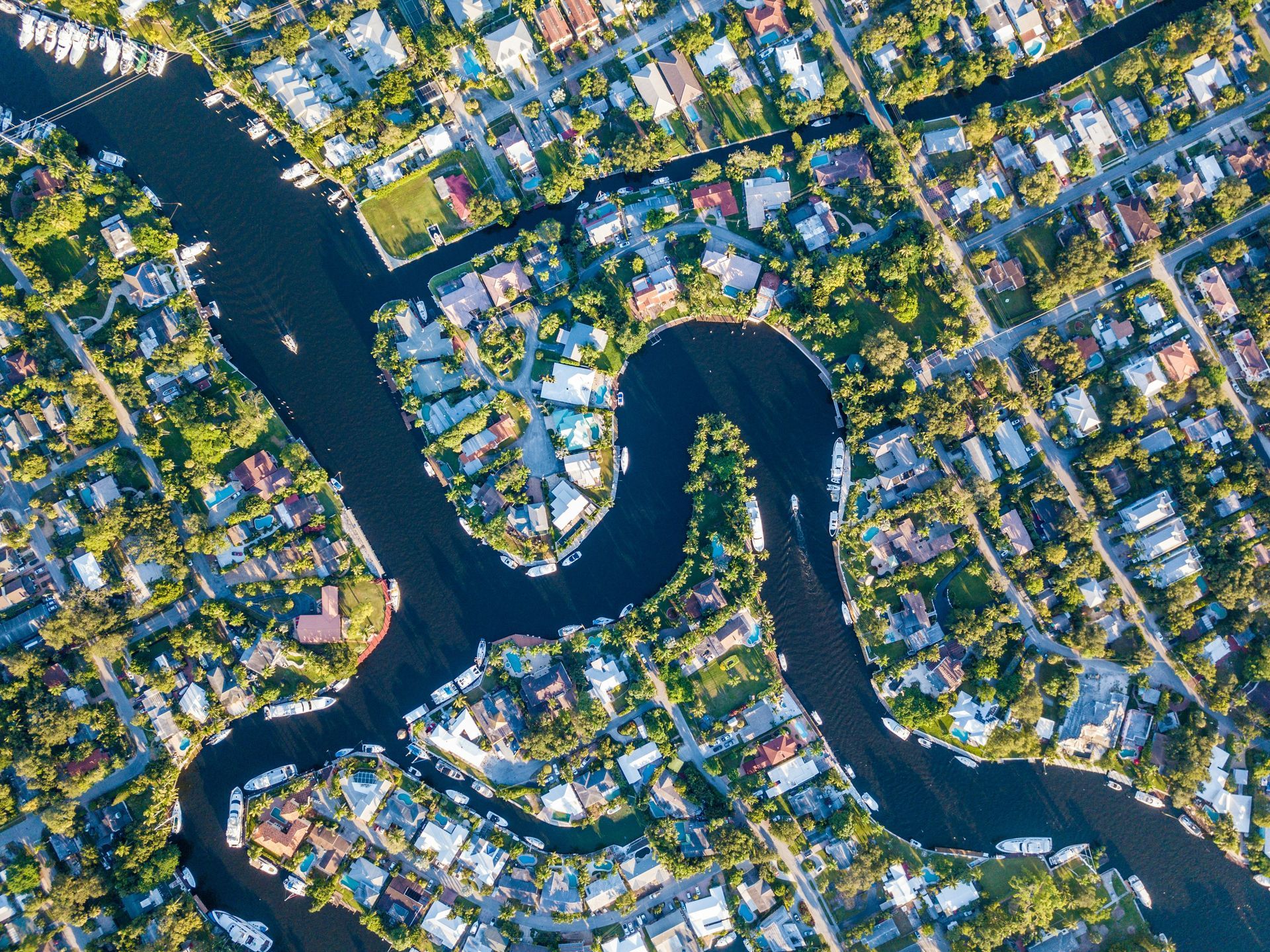 Aerial view of a winding waterway lined with houses and docks, with some boats visible.