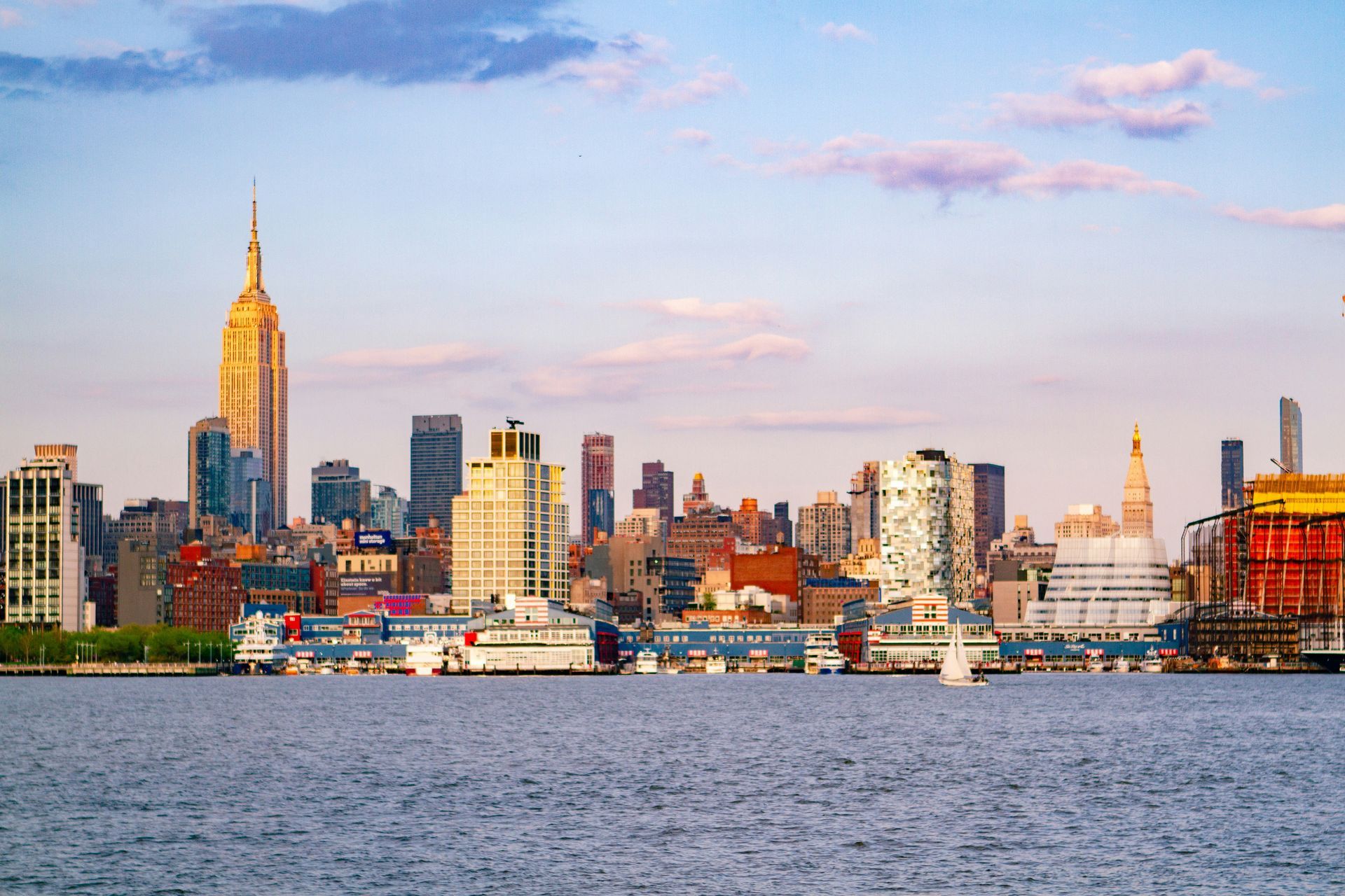 New York City skyline at sunset, with Empire State Building prominent. Water in foreground.