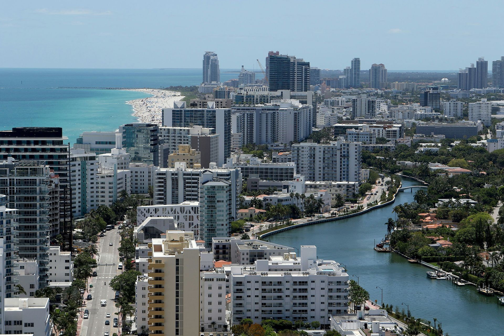 Coastal cityscape with high-rise buildings, beach, and waterway under a clear blue sky.