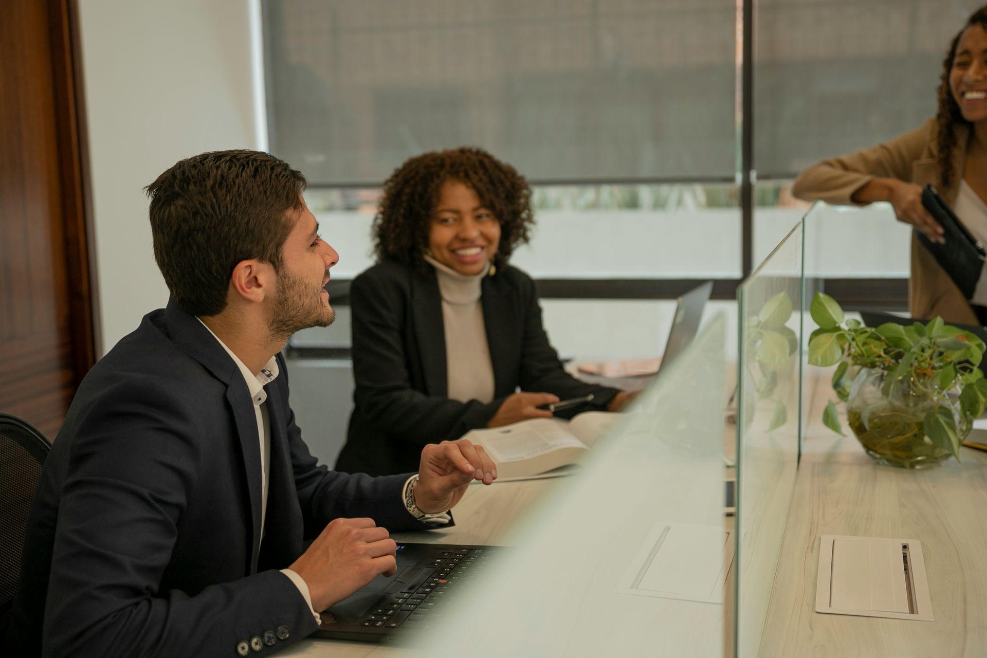 Man with glasses, writing at desk near a window. A small wind turbine model and a cup of coffee are on the table.